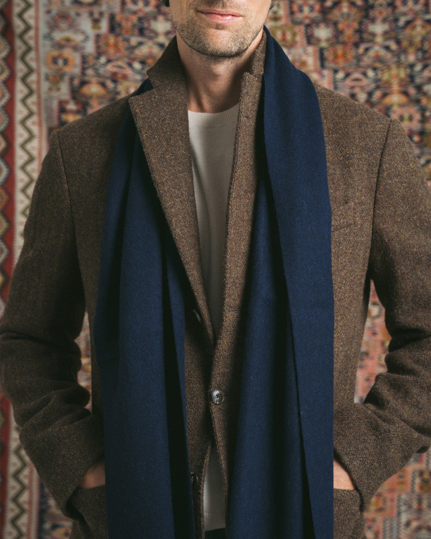 A close-up of a man wearing a navy wool scarf draped over a brown blazer and cream sweater.