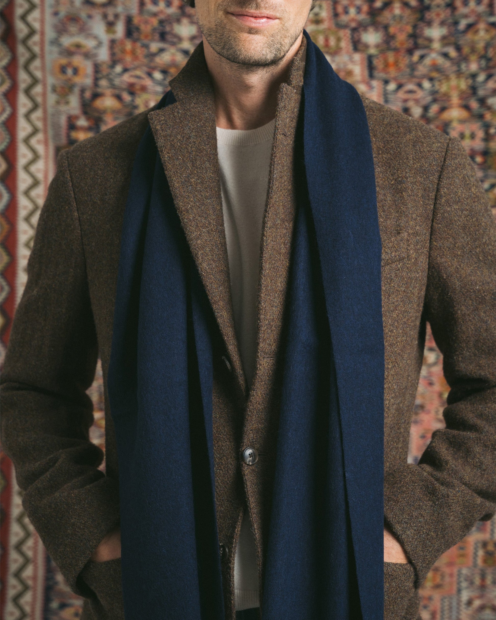 A close-up of a man wearing a navy wool scarf draped over a brown blazer and cream sweater.