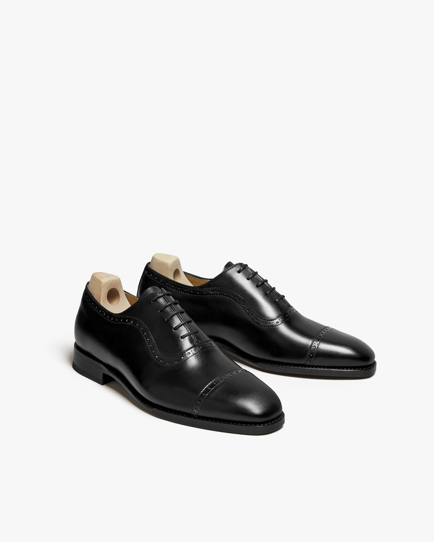 Skytteholm II in black calf, a pair of classic Oxford dress shoes with closed lacing, gently chiseled toes, and subtle brogue detailing, shown with wooden shoe trees and a polished finish.