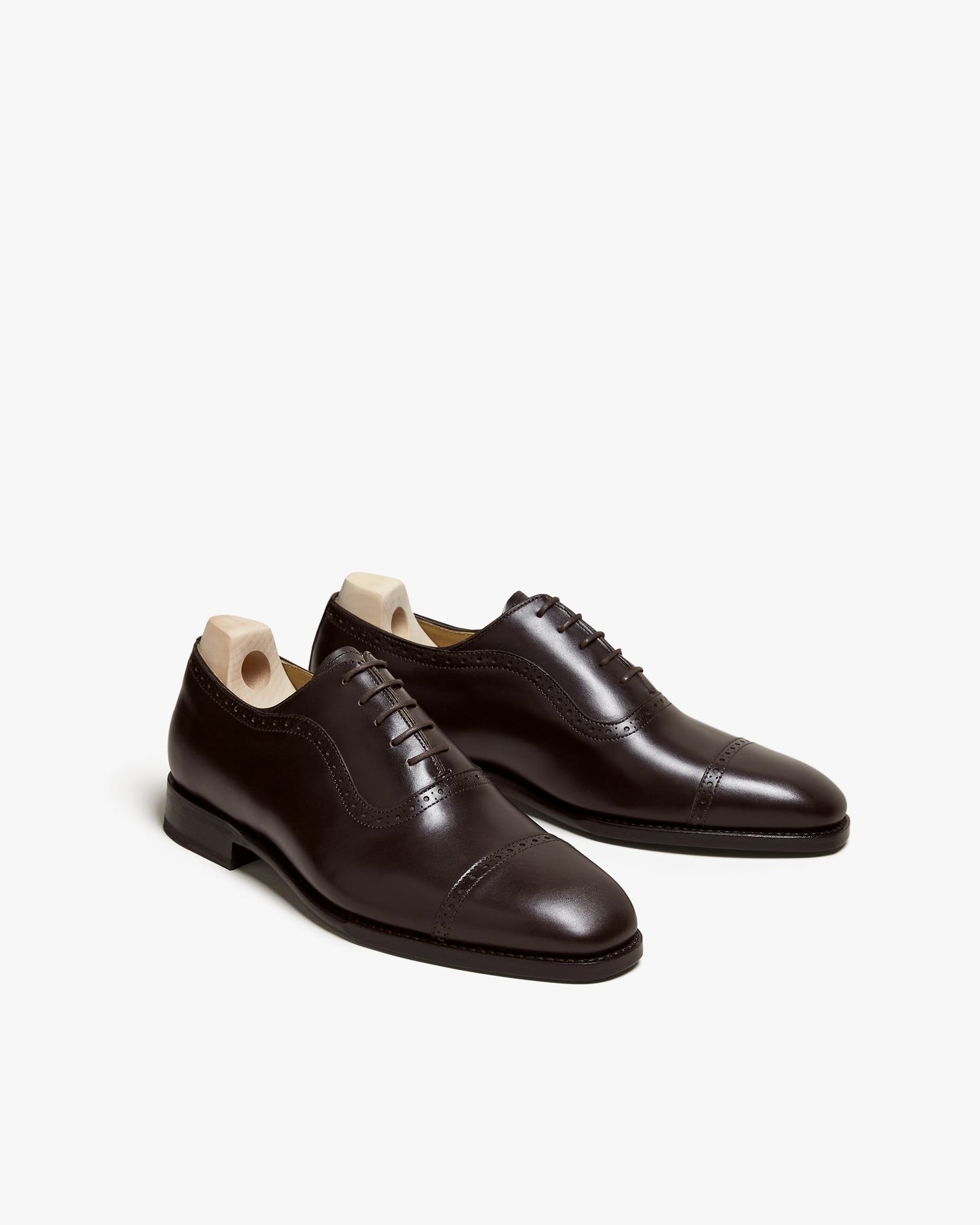 Pair of Skytteholm II oxford shoes in dark brown calf, featuring cap toes, subtle brogue accents, and closed lacing, displayed with wooden shoe trees to highlight their elegant shape and polished finish.