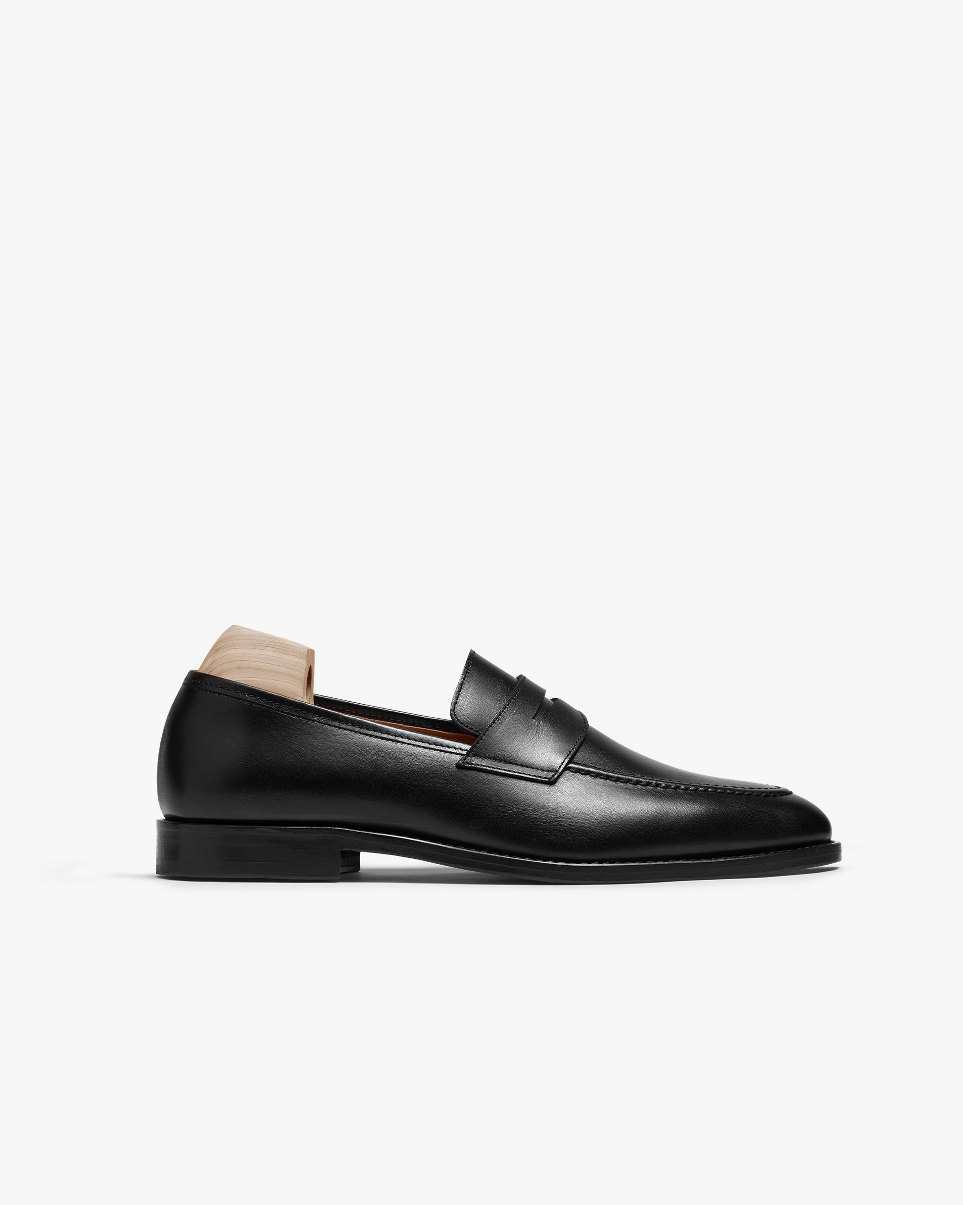 Smögen loafer in black calf leather features a gently rounded toe, classic penny strap, and smooth full-grain finish, shown in profile with a wooden shoe tree inserted.