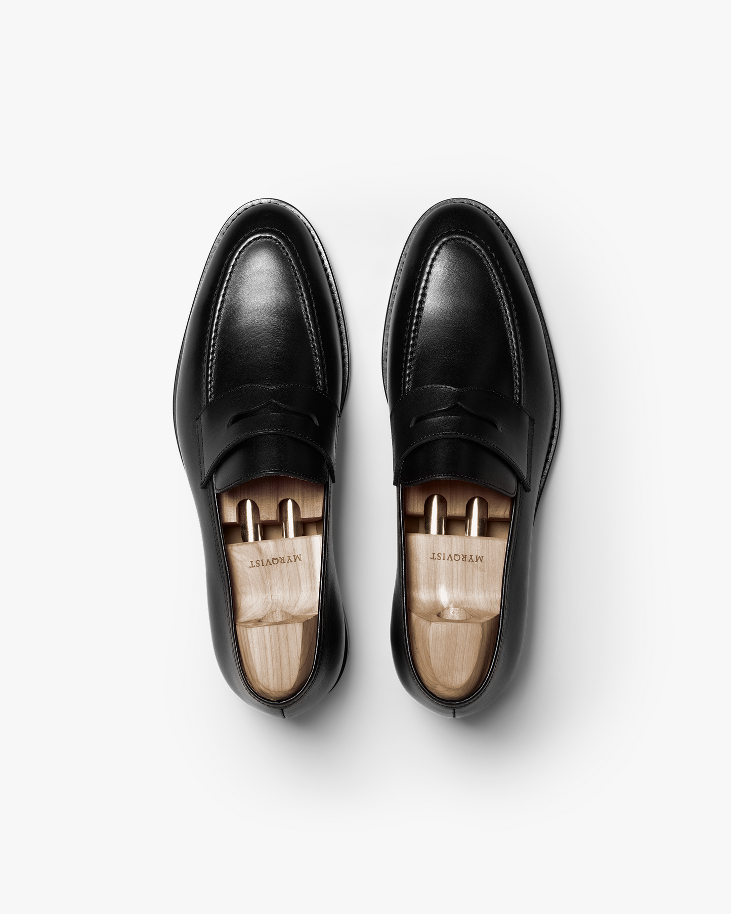 Pair of Smögen loafers in black calf leather shown from above, highlighting the clean lines, classic penny strap, and smooth finish with wooden shoe trees inside each shoe.