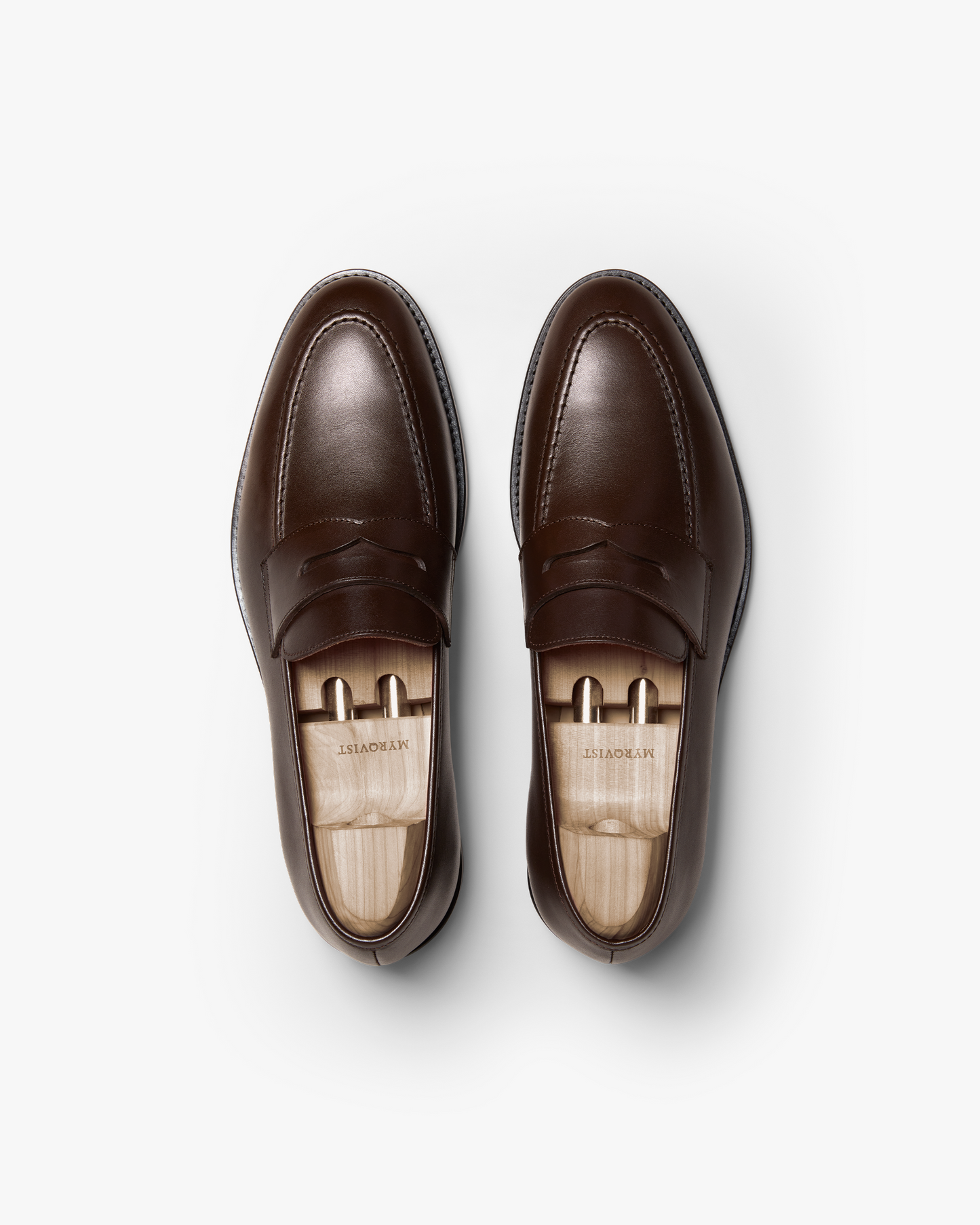 Pair of Smögen loafers in dark brown calf leather shown from above, highlighting the classic penny strap, gently rounded toe, and smooth, polished finish with wooden shoe trees inside.