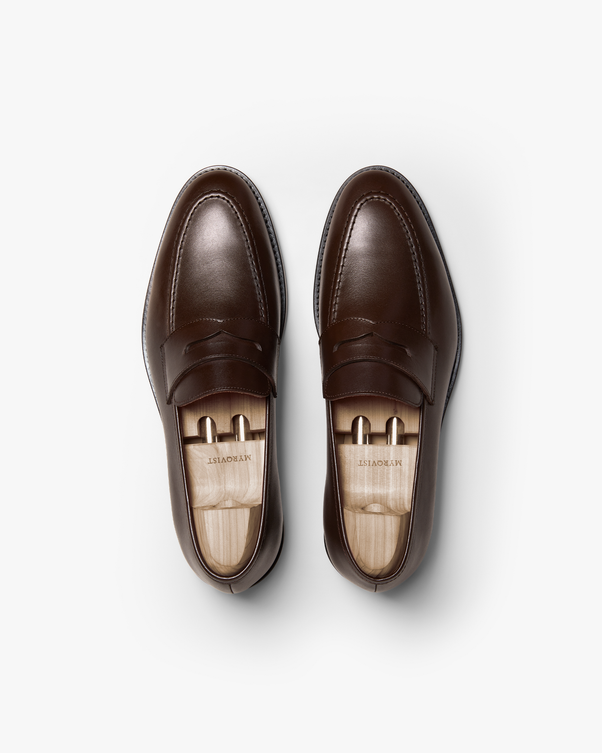 Pair of Smögen loafers in dark brown calf leather shown from above, highlighting the classic penny strap, gently rounded toe, and smooth, polished finish with wooden shoe trees inside.