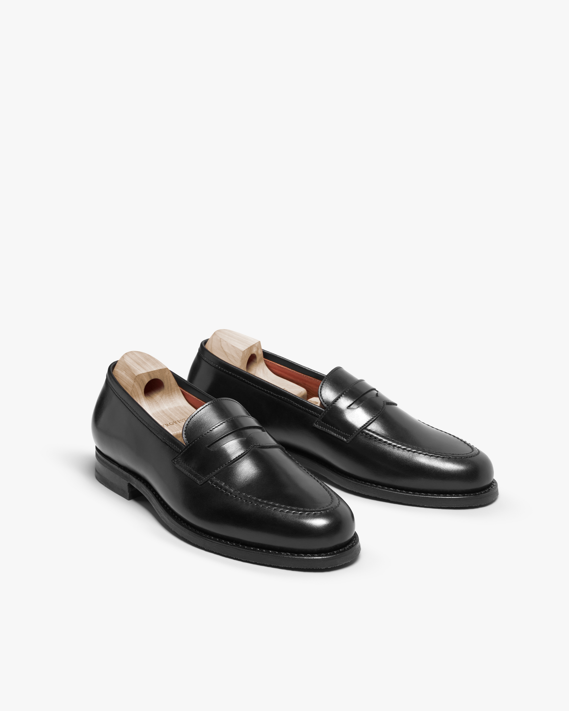 Stenhammar II in black calf displayed at an angle, featuring polished full-grain leather, apron stitching, penny strap detailing, and wooden shoe trees to preserve the loafer’s elegant shape.