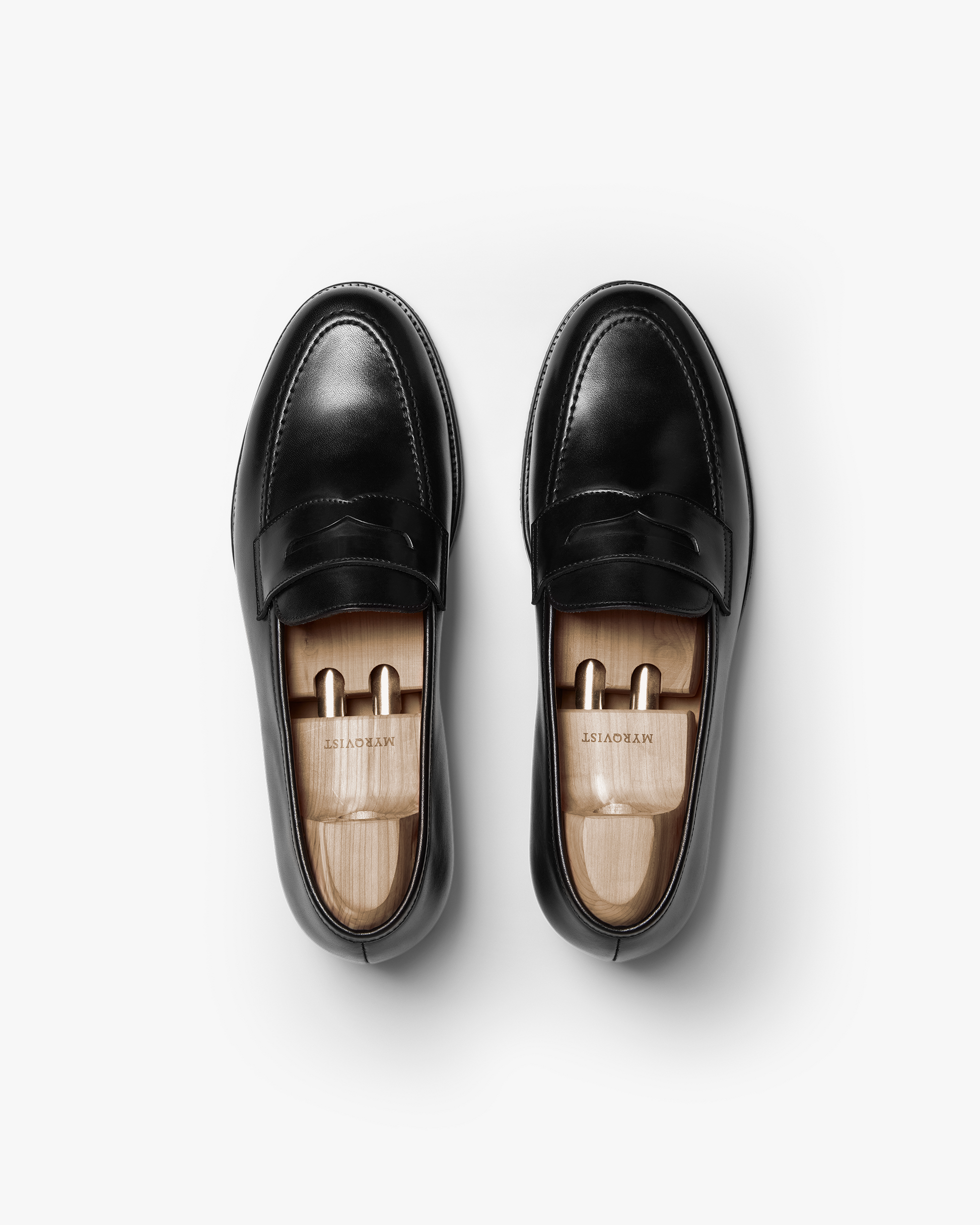 A pair of Stenhammar II in black calf shown from above, highlighting the polished penny loafer design, apron stitching, and wooden shoe trees inside each shoe for shape retention.