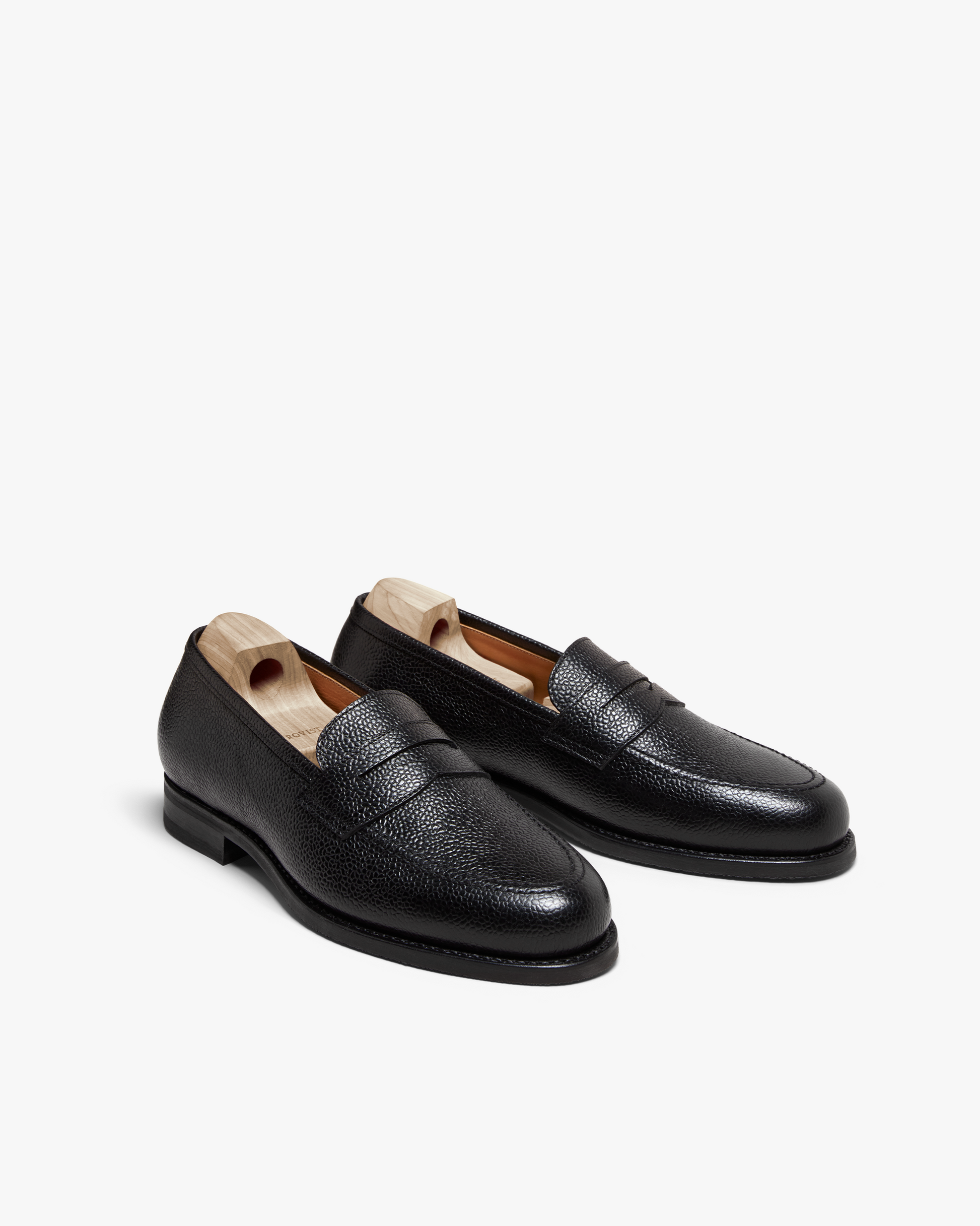 Stenhammar II in black country calf shown at an angle, highlighting the textured grain leather, classic penny strap, apron toe, and wooden shoe trees inside each loafer.