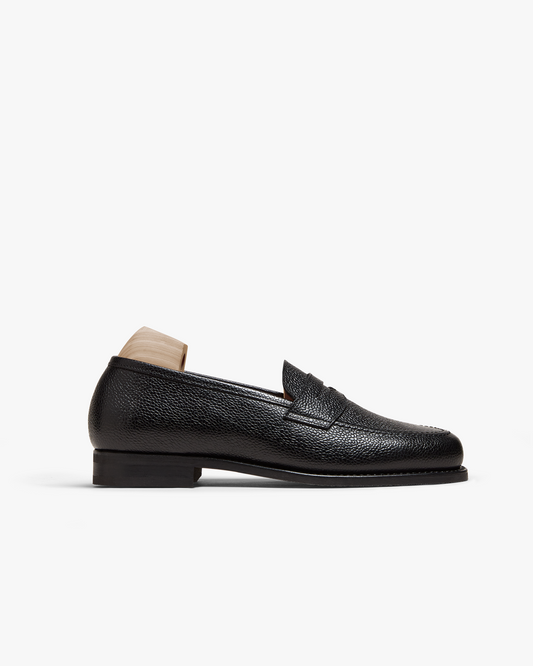 Stenhammar II in black country calf displayed in profile, highlighting its textured grain leather, classic penny strap, apron toe, and stacked heel with a wooden shoe tree inserted.