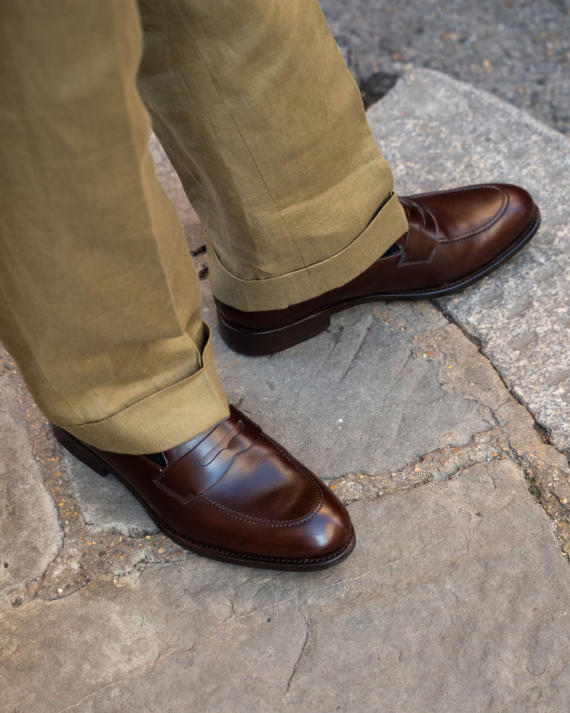 Stenhammar II in dark brown calf worn with light brown slacks, highlighting the smooth full-grain leather, apron stitching, and classic penny loafer style in an outdoor setting.