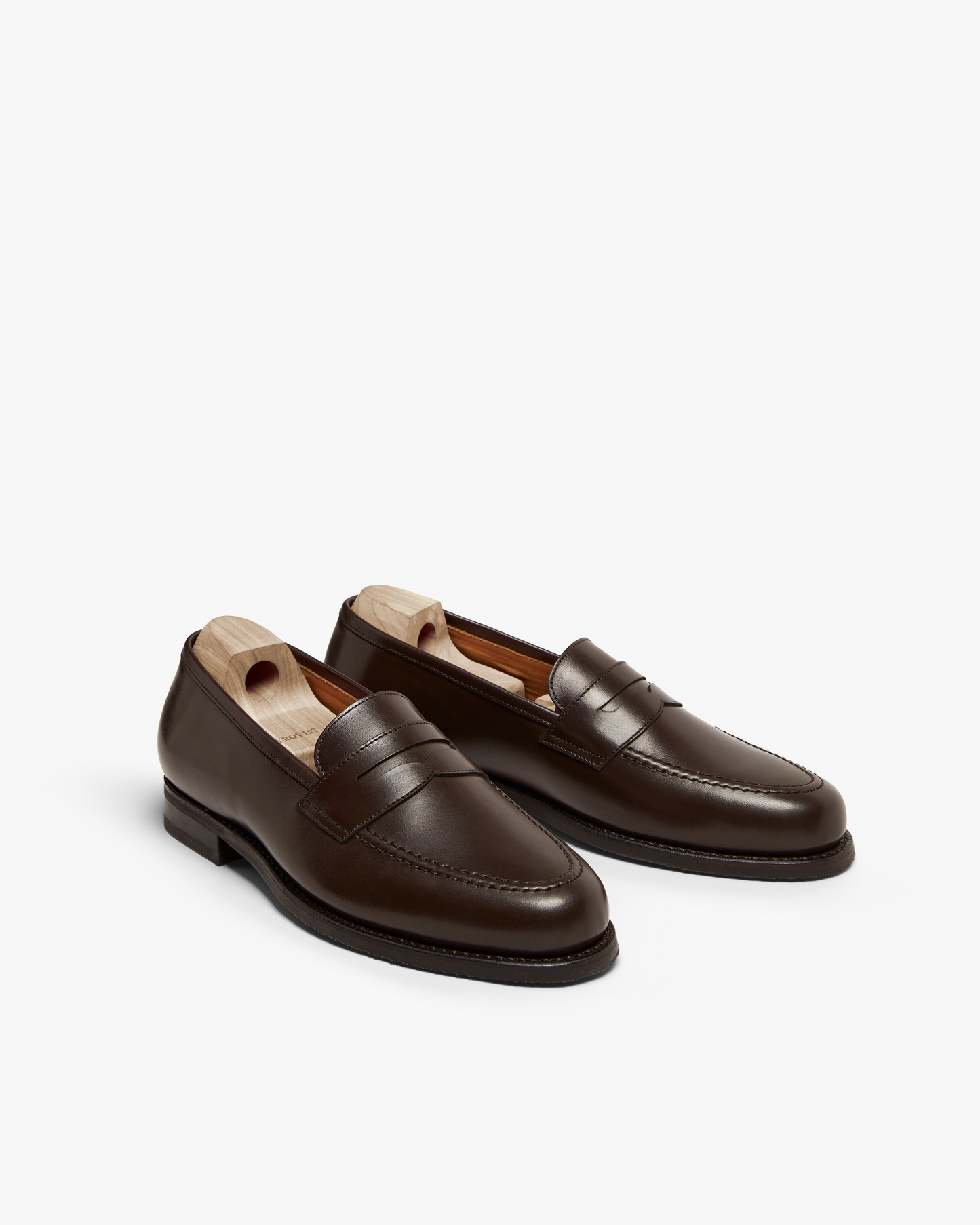 Stenhammar II in dark brown calf, shown at an angle to highlight the smooth full-grain leather, apron stitching, and classic penny loafer silhouette, each shoe fitted with a wooden shoe tree.