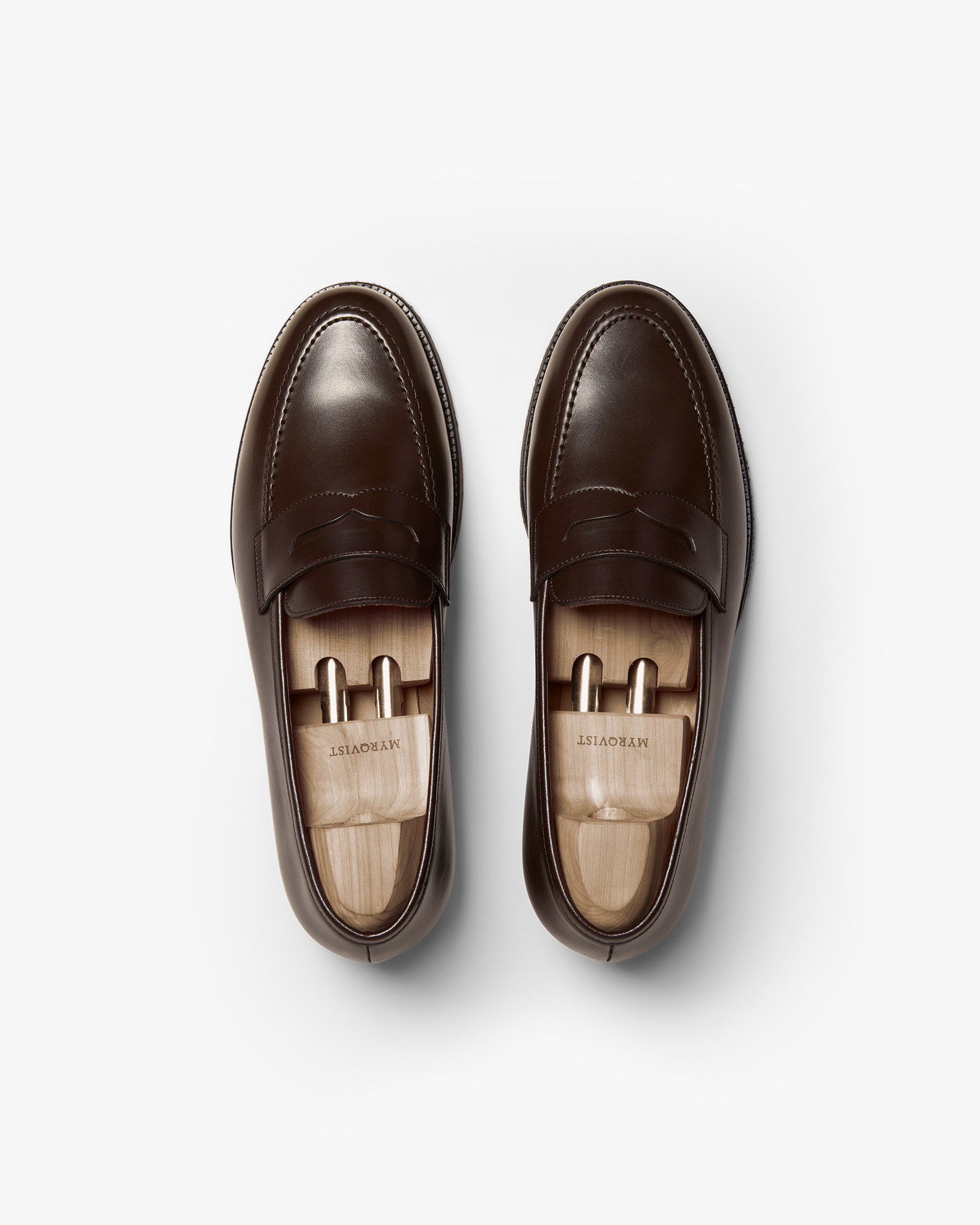 A pair of Stenhammar II in dark brown calf, featuring smooth full-grain leather with apron stitching and wooden shoe trees inserted, shown from above to highlight the classic penny loafer design.