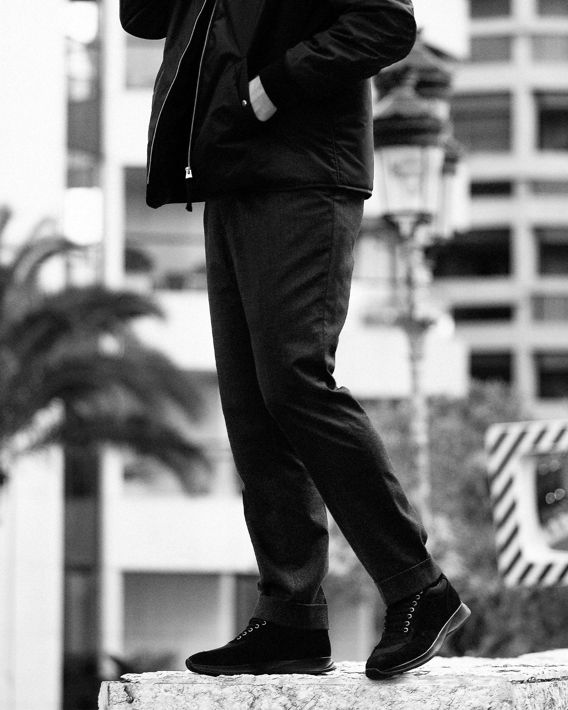 A man wearing Stensund in black suede with tailored slacks and a jacket stands confidently outdoors, highlighting the trainer’s clean silhouette and versatile style for both business casual and relaxed city settings.