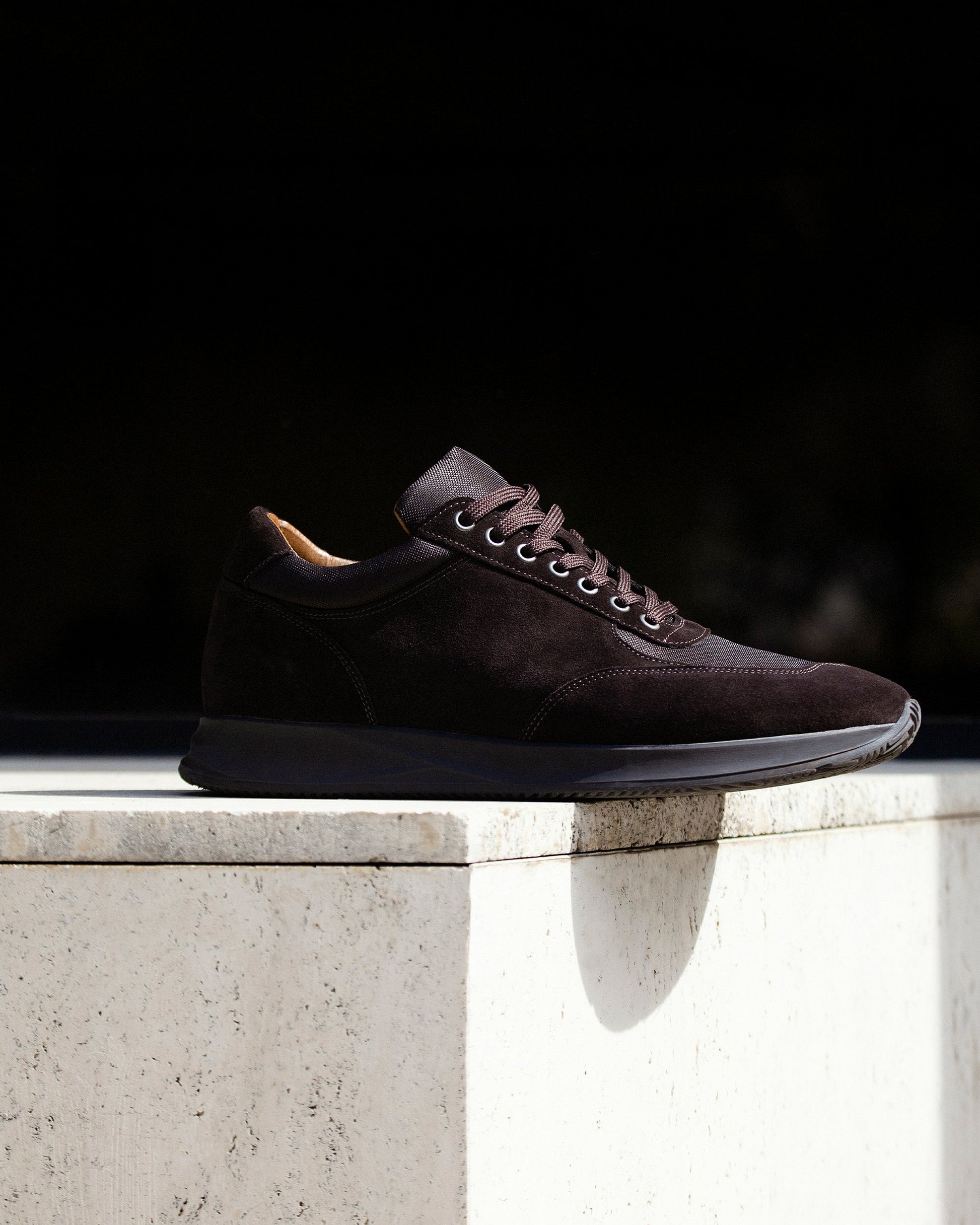 Stensund in dark brown suede displayed on a light stone surface, showcasing its smooth suede upper, tonal mesh accents, and sculpted rubber sole in natural sunlight.