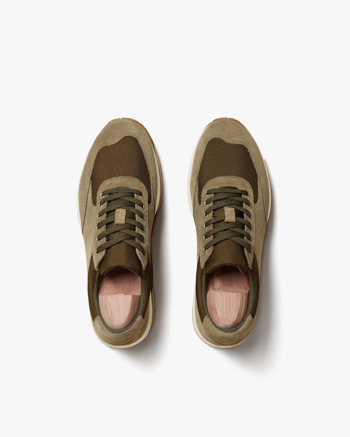 Stensund in moss green suede shown from above, highlighting the tonal mesh panels, lace-up closure, and softly rounded toe with off-white soles and wooden shoe trees inside each sneaker.
