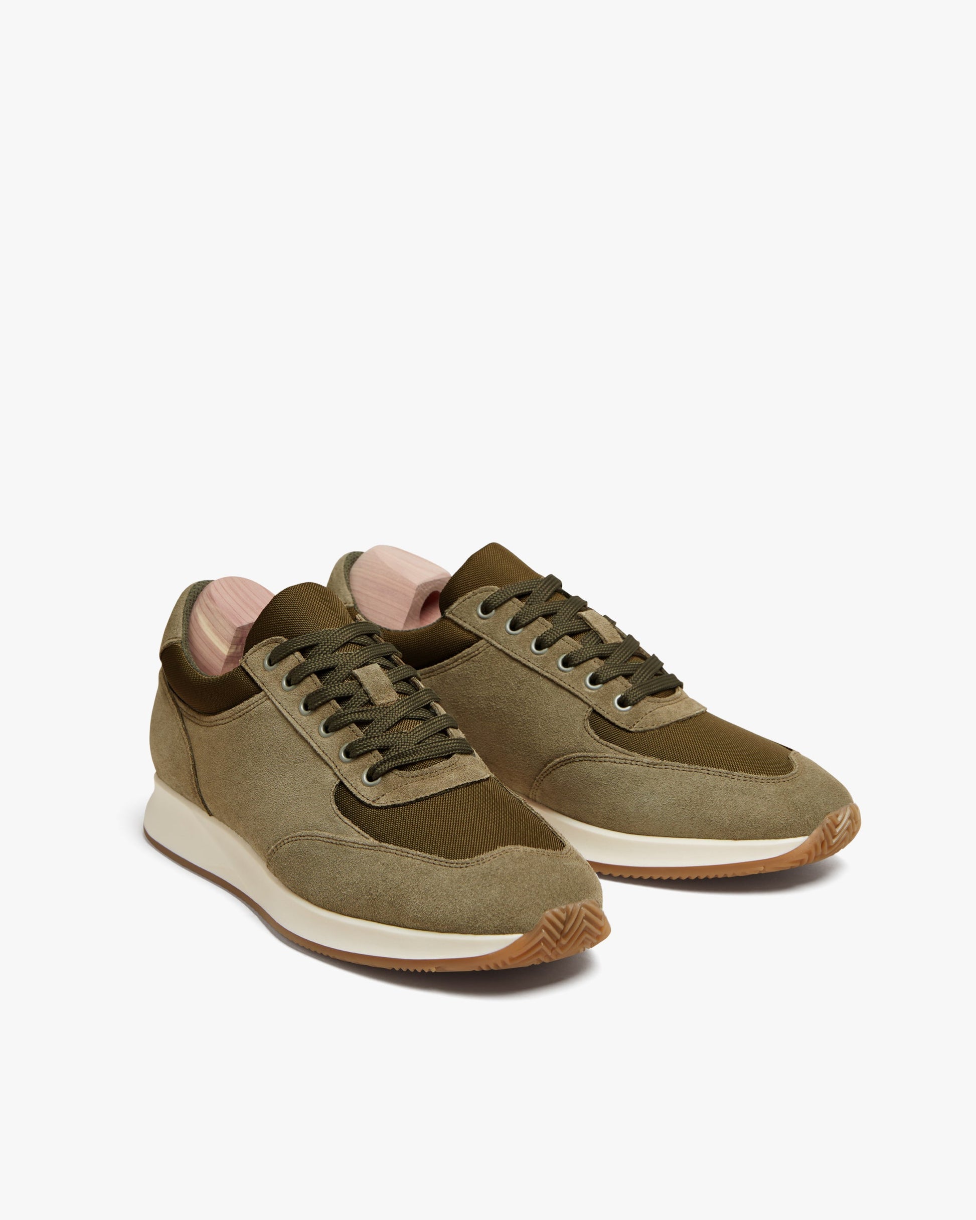 Stensund in moss green suede features a pair of lace-up sneakers with tonal mesh panels, off-white midsoles, gum rubber outsoles, and wooden shoe trees, highlighting a modern Scandinavian design.
