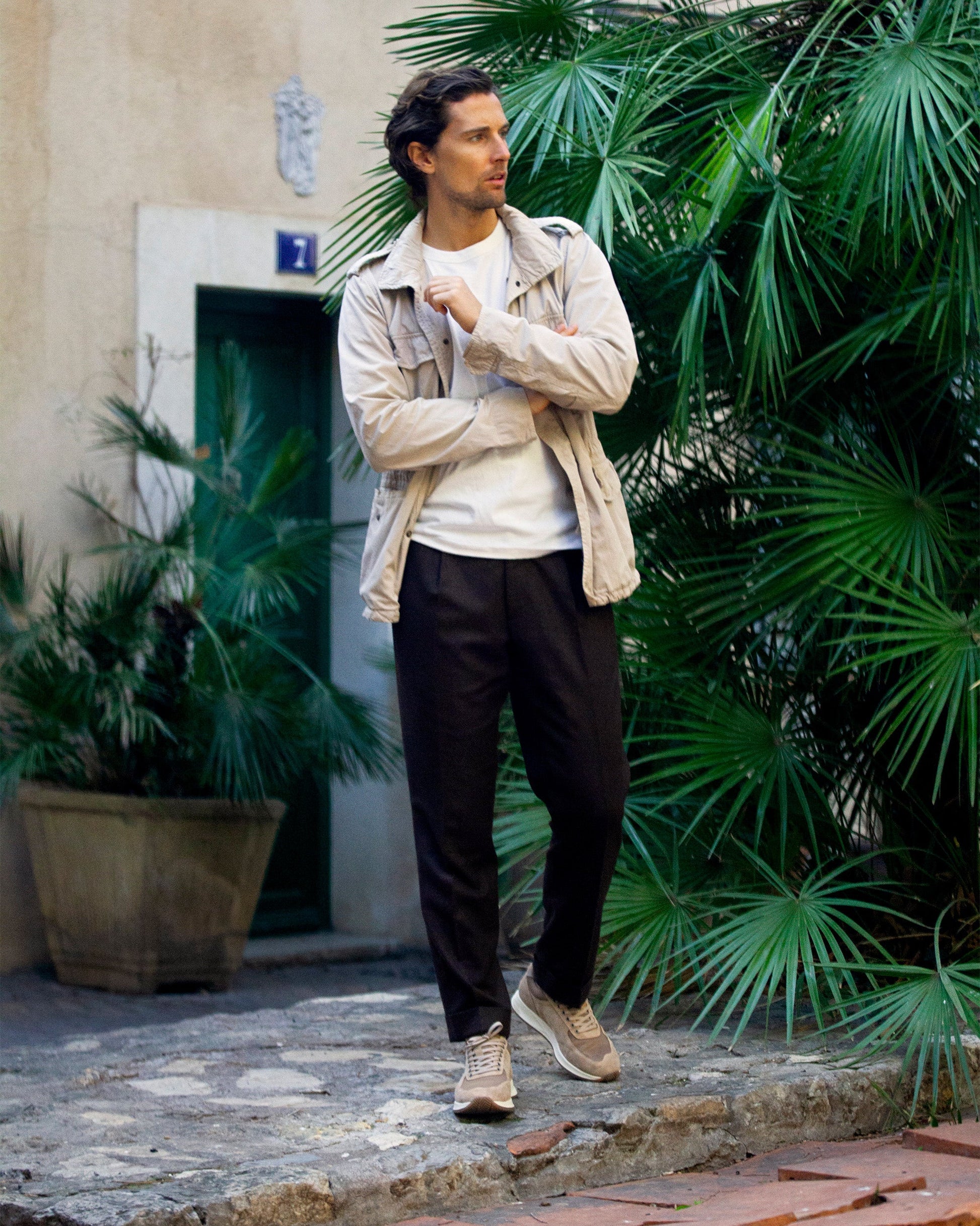 A man walks outdoors in Stensund in sand suede, paired with brown slacks, a white shirt, and a light jacket, showcasing the trainer's soft beige suede and versatile style for both business casual and relaxed settings.