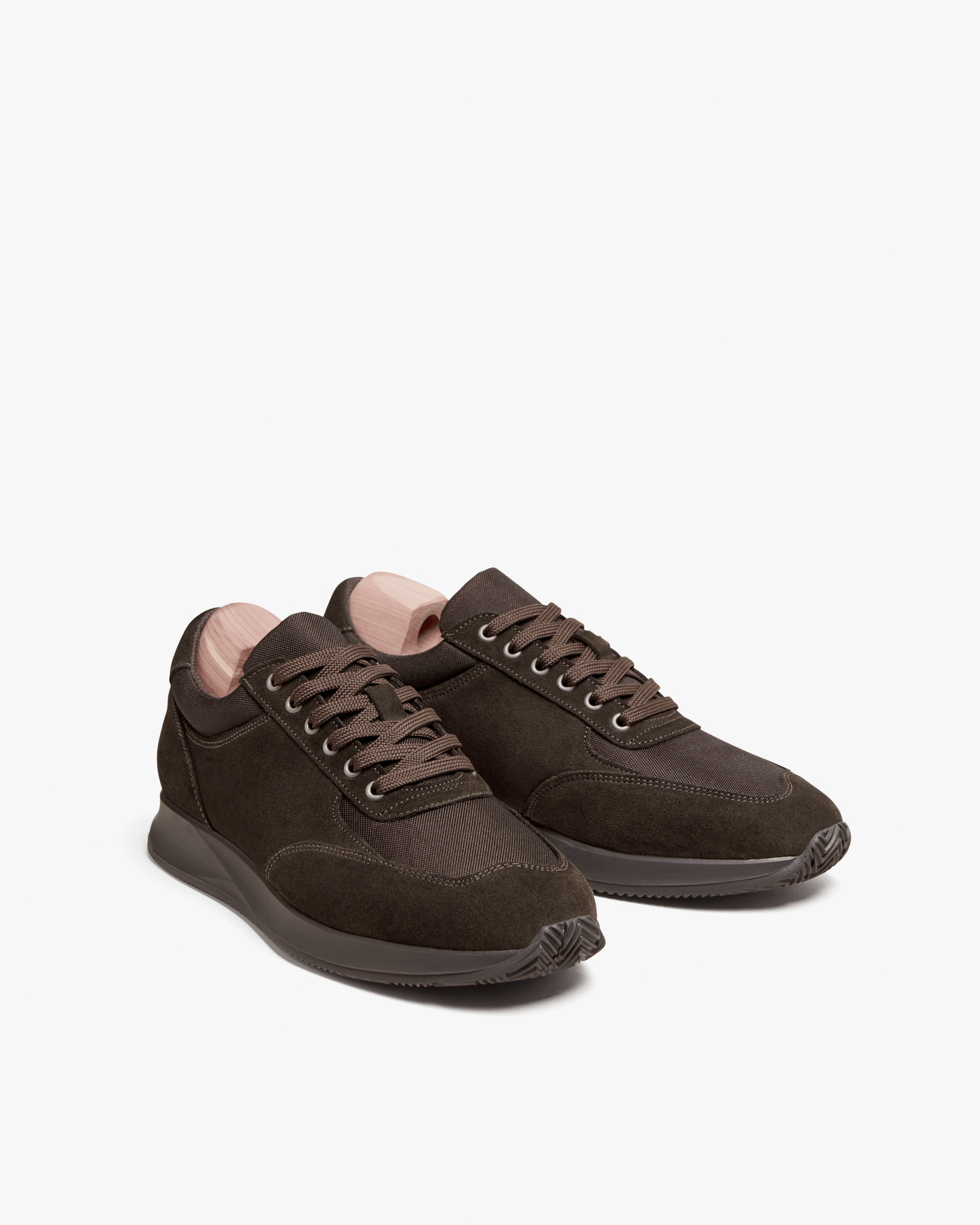 Stensund in dark brown suede features a modern low-top silhouette with tonal mesh panels, matching brown laces, and sculpted rubber soles, presented with wooden shoe trees for shape and care.