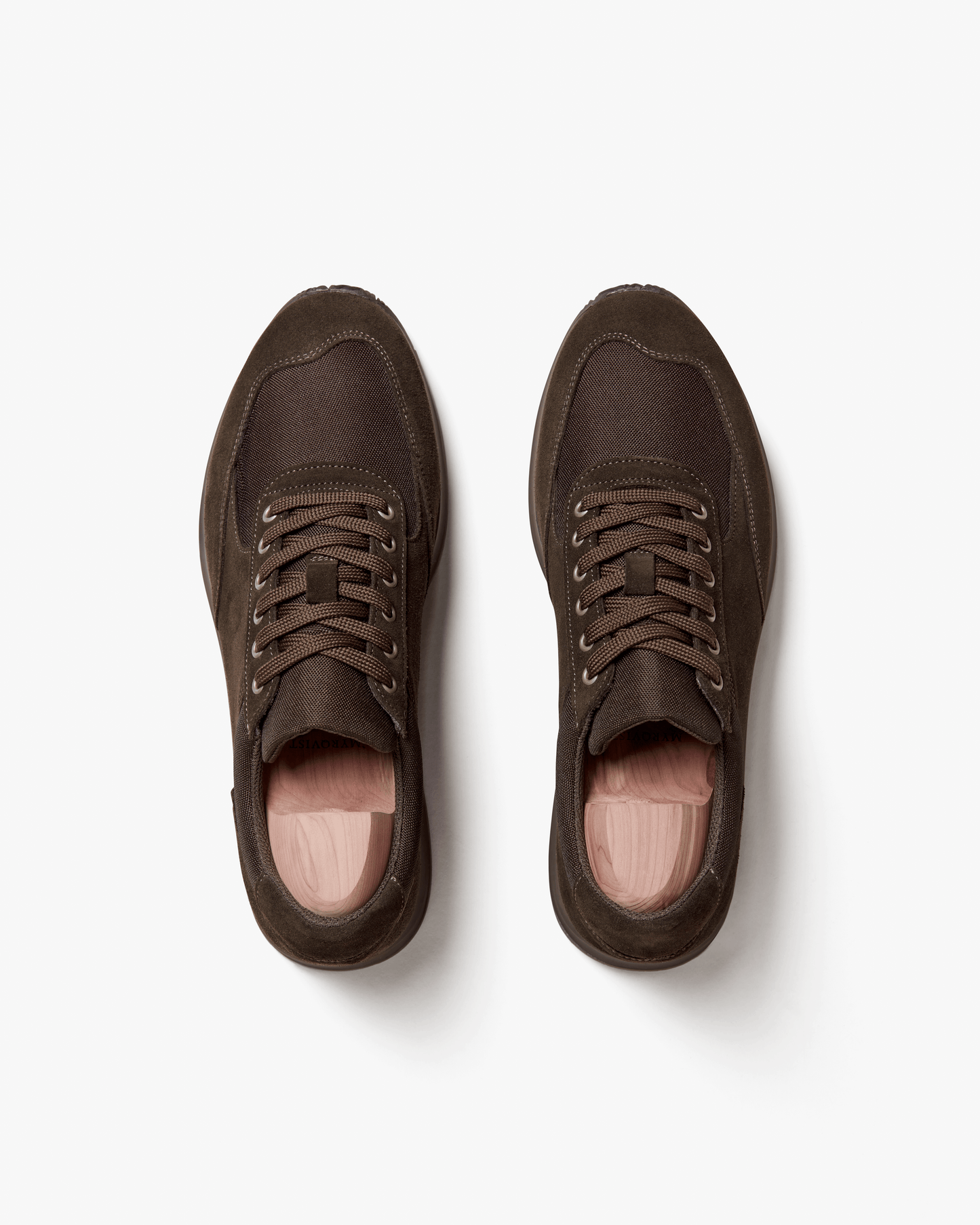 Stensund in dark brown suede shown from above, highlighting the smooth suede panels, tonal mesh details, matching brown laces, and wooden shoe trees inside each sneaker.