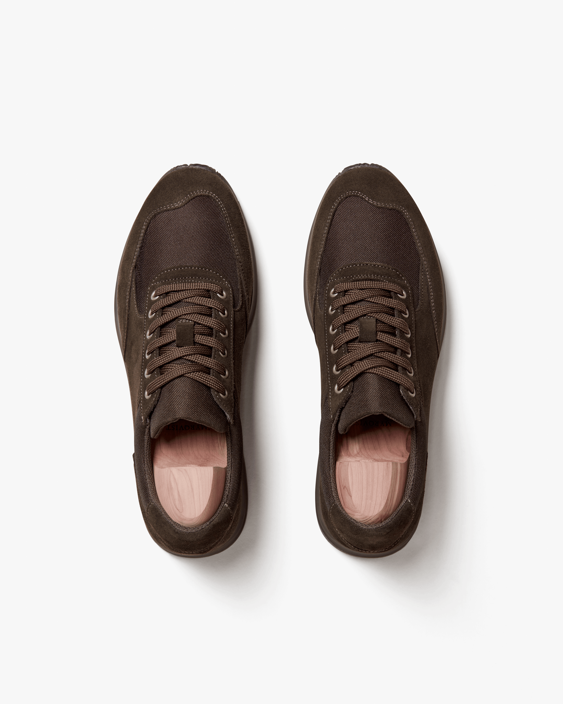 Stensund in dark brown suede shown from above, highlighting the smooth suede panels, tonal mesh details, matching brown laces, and wooden shoe trees inside each sneaker.