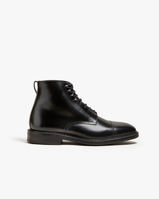 Tjärnö II in black calf shown in side profile, featuring a polished men’s boot with a cap toe, subtle broguing, lace-up fastening with metal eyelets, and a clean, refined silhouette that highlights the smooth leather finish.