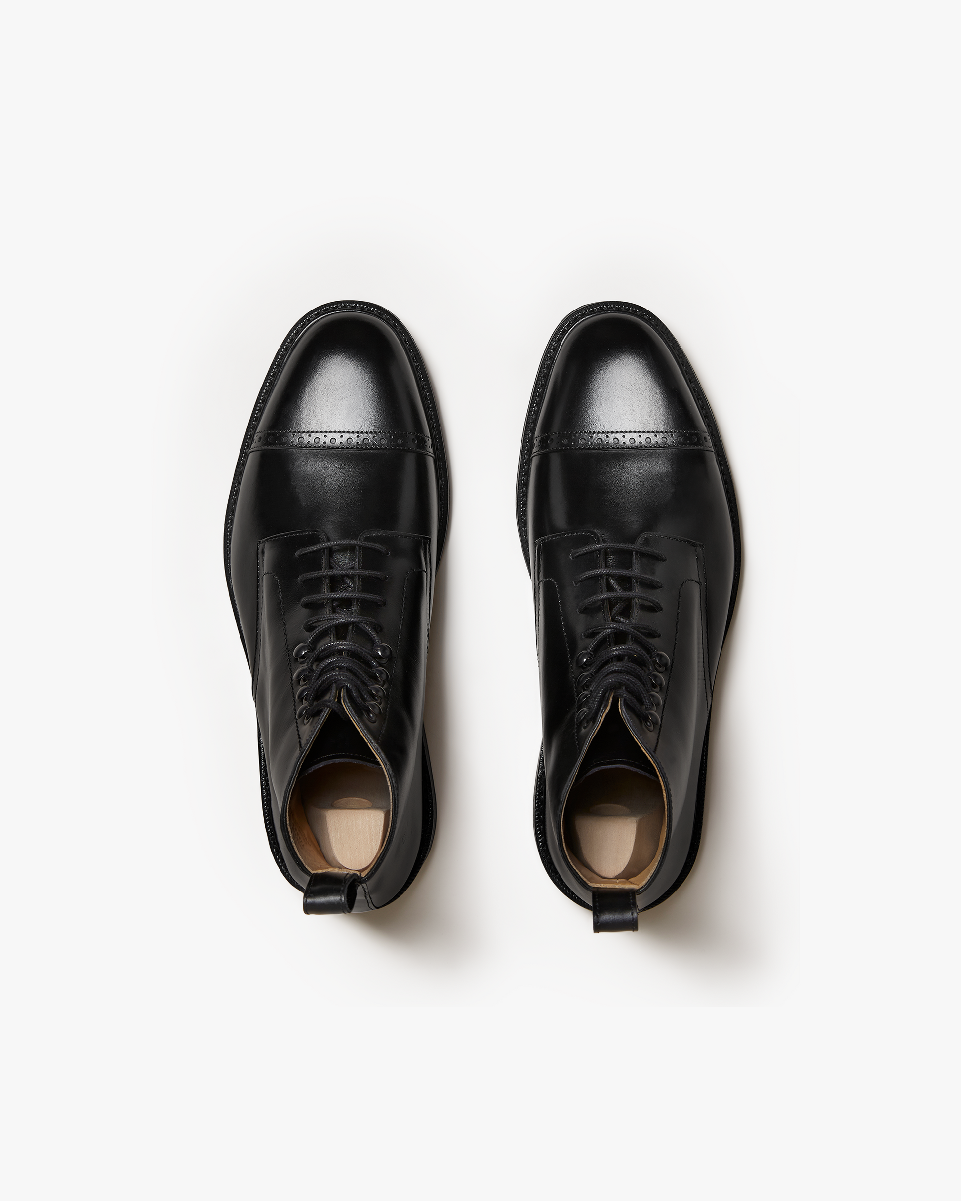 Tjärnö II in black calf features a pair of polished men's boots with cap toes, subtle broguing, lace hooks, and pull tabs, shown from above to highlight their refined silhouette and smooth leather finish.