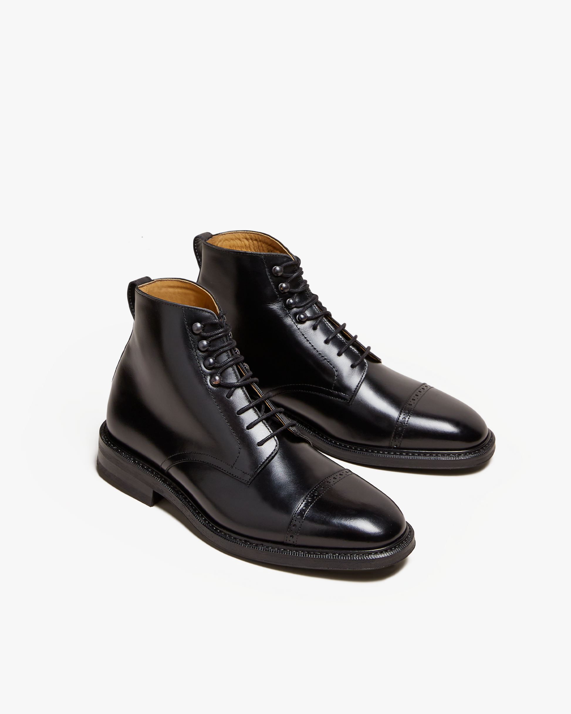 Tjärnö II in black calf features a pair of polished men's boots with cap toes, subtle broguing, lace hooks, and a rounded silhouette, designed for versatility and refined style.