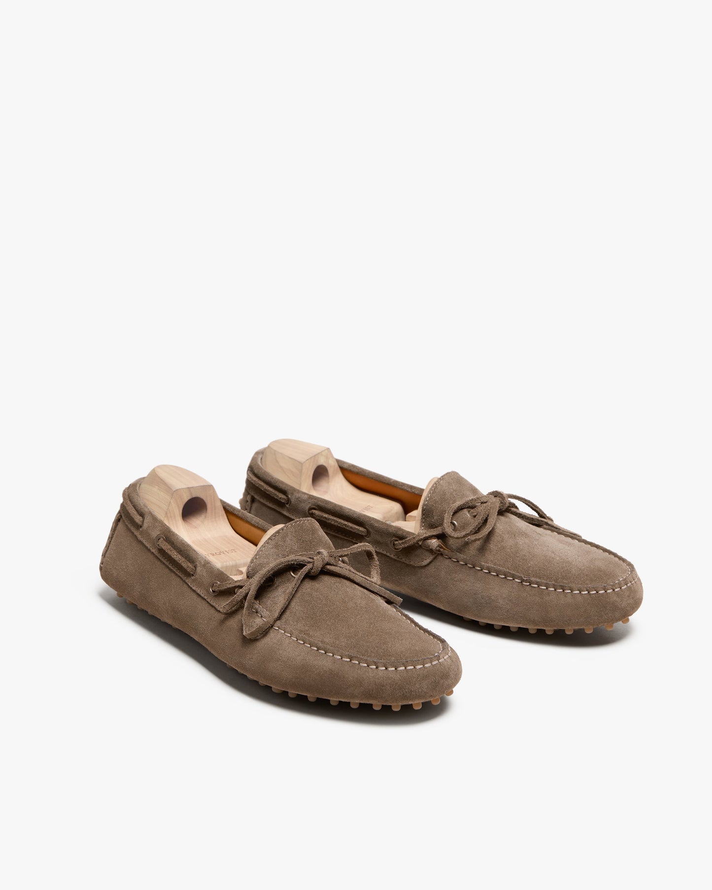 Tofta loafers in taupe suede with a rubber driving sole, tonal stitching, and bow detail, displayed at an angle with wooden shoe trees to maintain their shape.