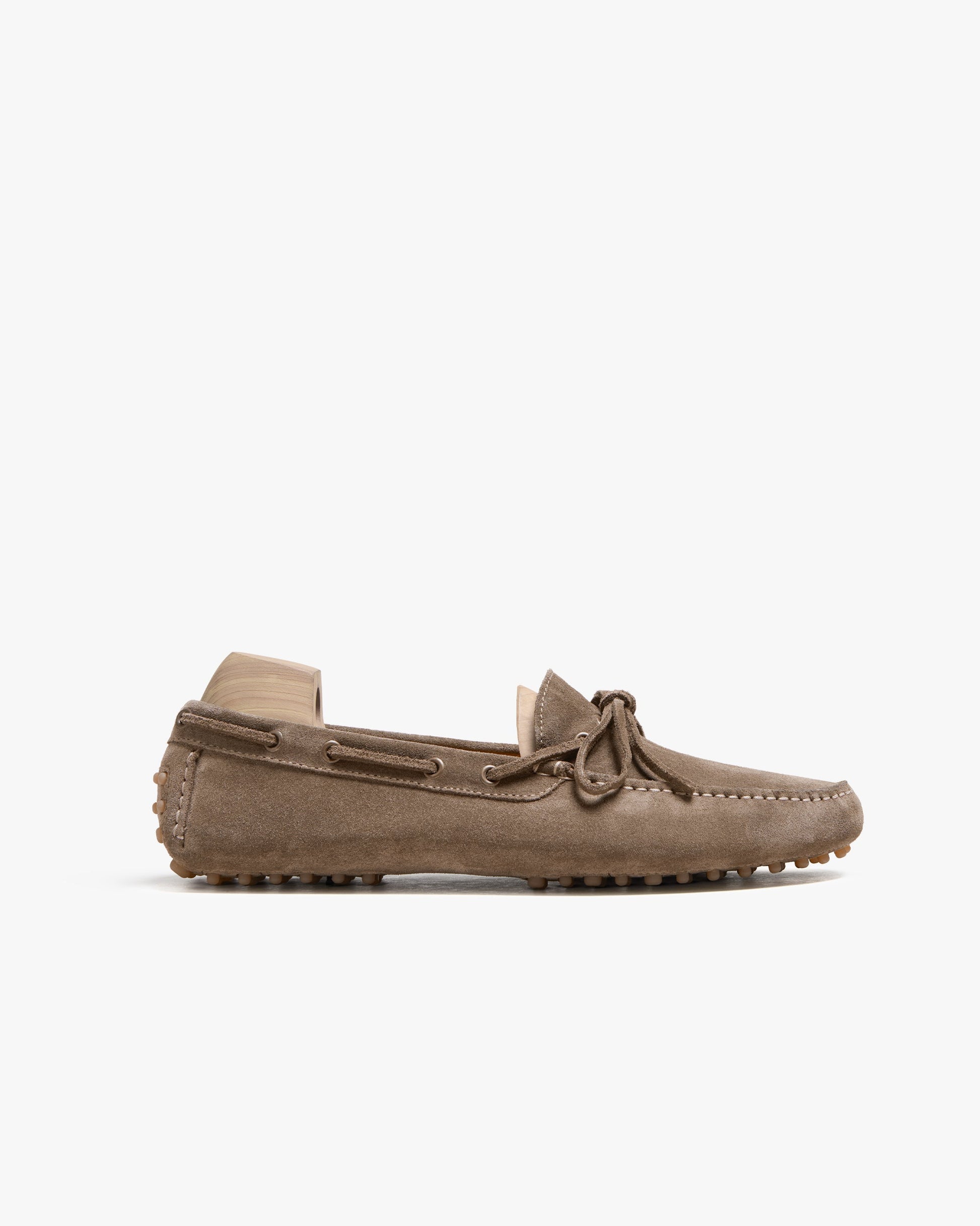 Taupe suede loafer with a driving sole, tonal stitching, and a subtle bow detail, shown in profile to highlight its soft texture and relaxed, flexible silhouette.