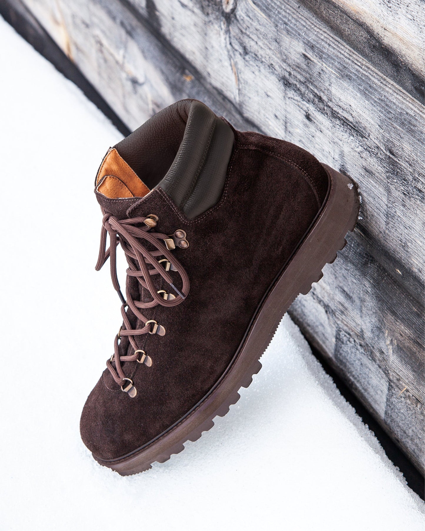 Duved in dark brown suede displayed outdoors on snow, featuring rich suede texture, brass-toned hardware, padded leather collar, and a rugged hiking sole designed for winter conditions.