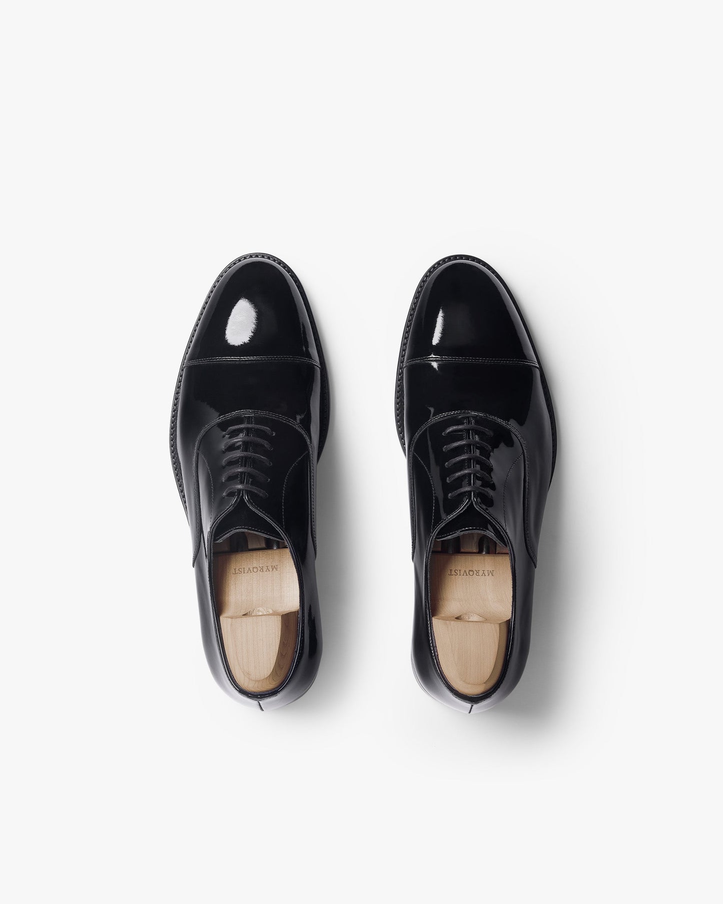 Pair of Vinterviken II oxford shoes in black patent leather, shown from above with a high-gloss finish, softly rounded cap toes, and wooden shoe trees inside each shoe.