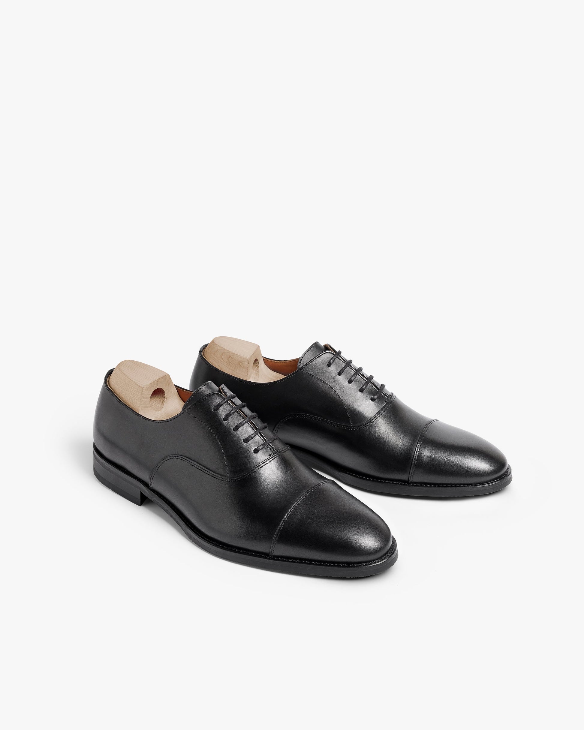 Vinterviken II oxford shoes in black calf, featuring a polished cap toe, clean stitching, and wooden shoe trees, displayed at an angle to highlight their elegant silhouette and craftsmanship.