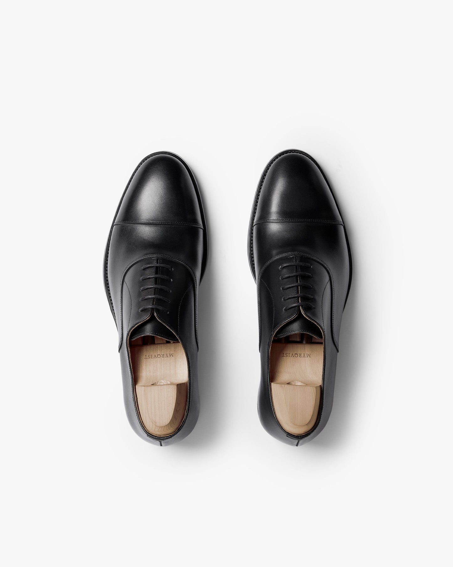 Pair of Vinterviken II oxford shoes in black calf, shown from above with polished cap toes, clean stitching, and wooden shoe trees inside each shoe.