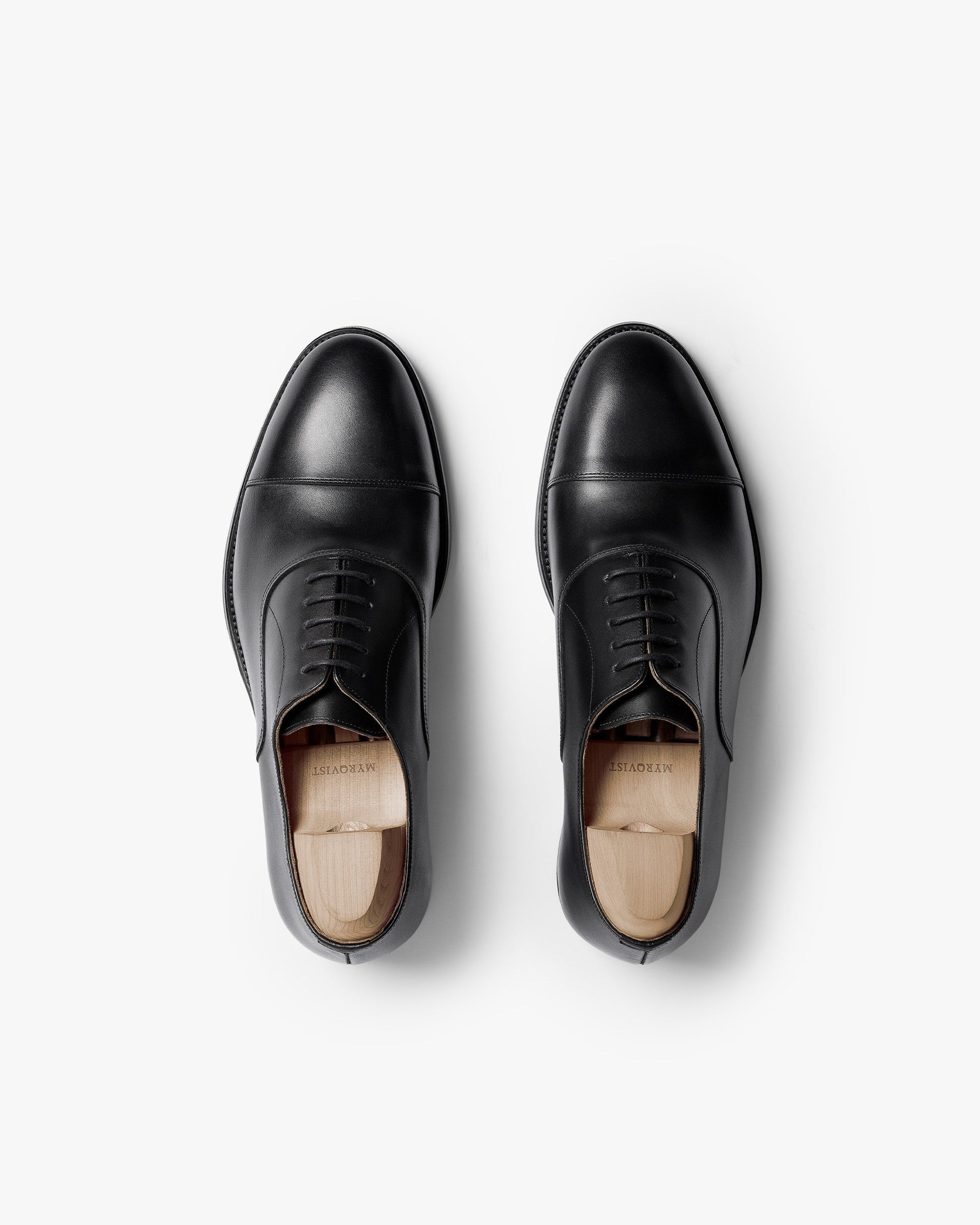Pair of Vinterviken II oxford shoes in black calf, shown from above with polished cap toes, clean stitching, and wooden shoe trees inside each shoe.