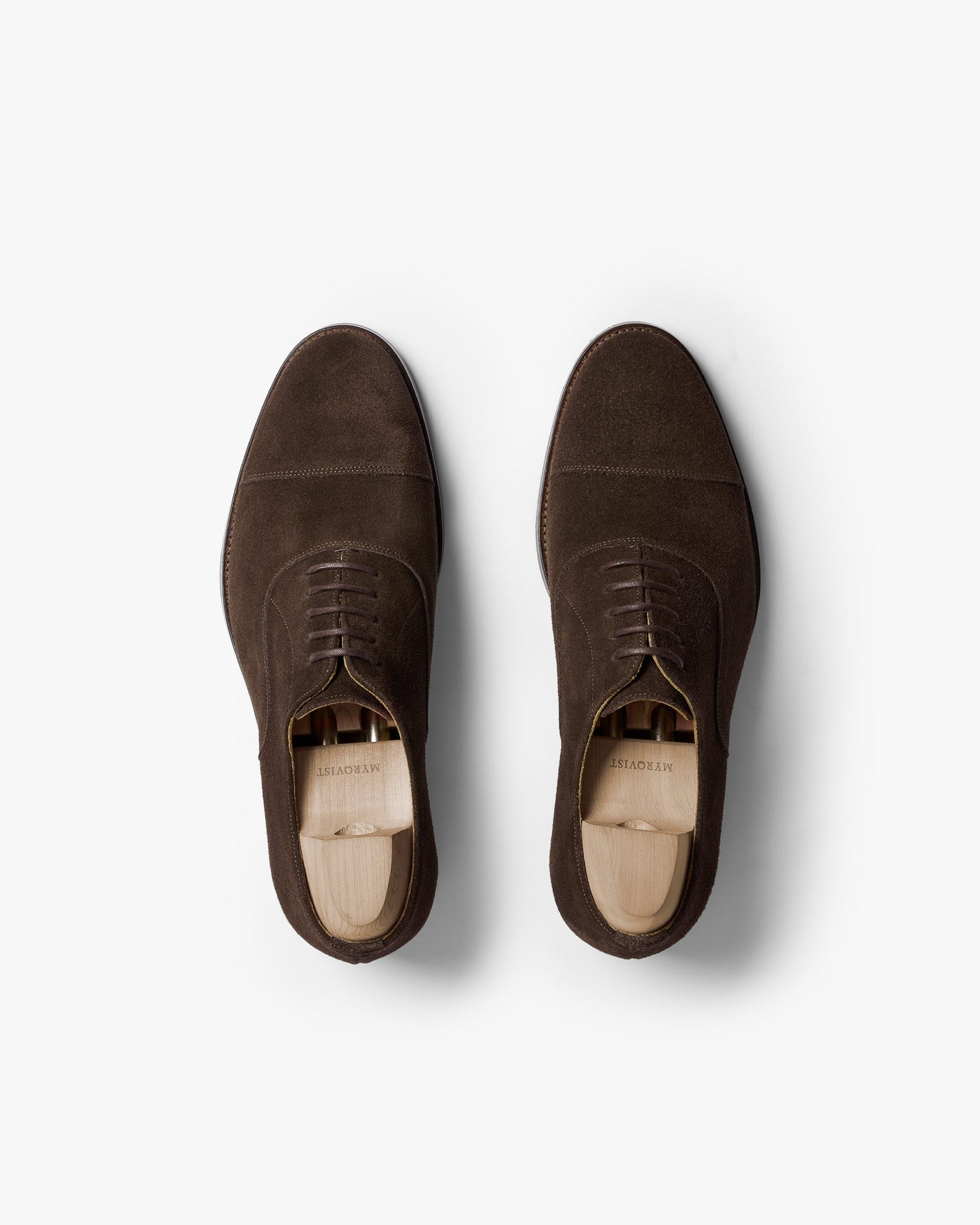 A pair of Vinterviken II oxford shoes in dark brown suede shown from above, highlighting the gently chiseled cap toe, clean stitching, and wooden shoe trees inside each shoe.