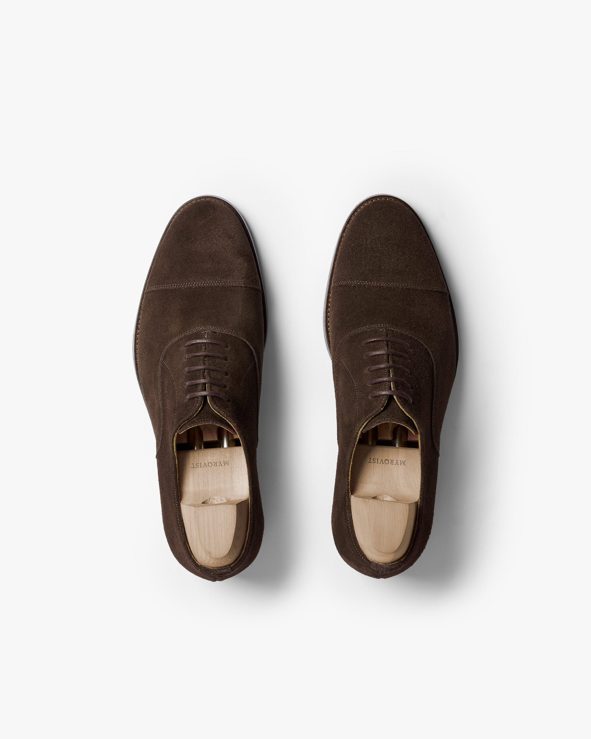 A pair of Vinterviken II oxford shoes in dark brown suede shown from above, highlighting the gently chiseled cap toe, clean stitching, and wooden shoe trees inside each shoe.