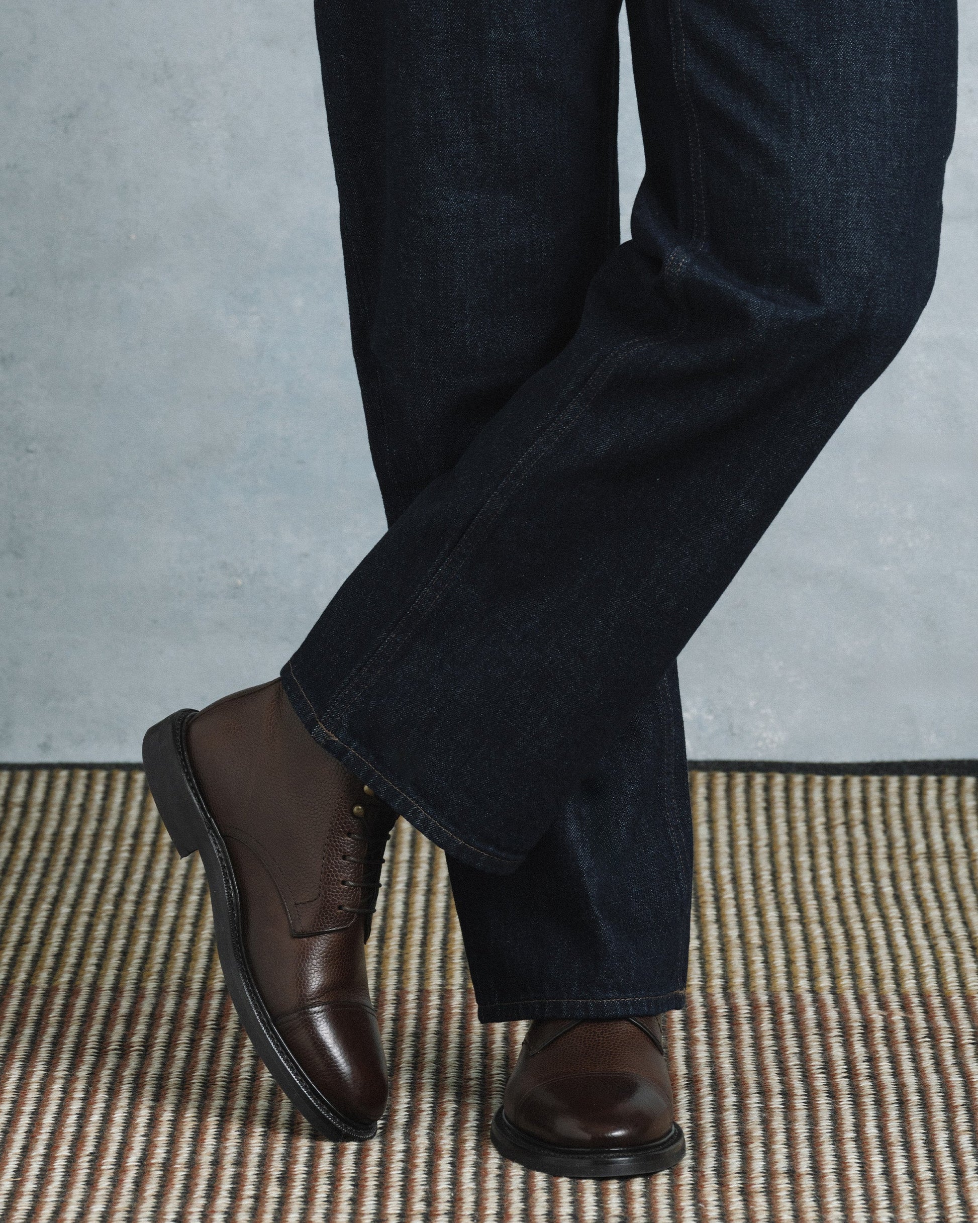 Abisko in dark brown country calf worn with dark denim, showcasing the textured grained leather, cap toe, and sturdy rubber sole for a refined yet versatile style suitable for both casual and dressed-up occasions.