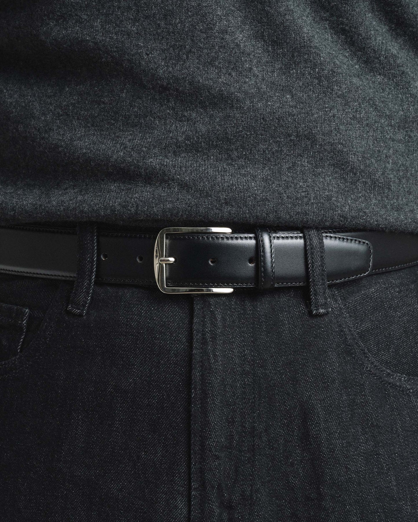 Black leather belt with a square silver buckle, styled with dark denim jeans and a charcoal sweater for a modern, understated look suitable for casual or smart-casual occasions.