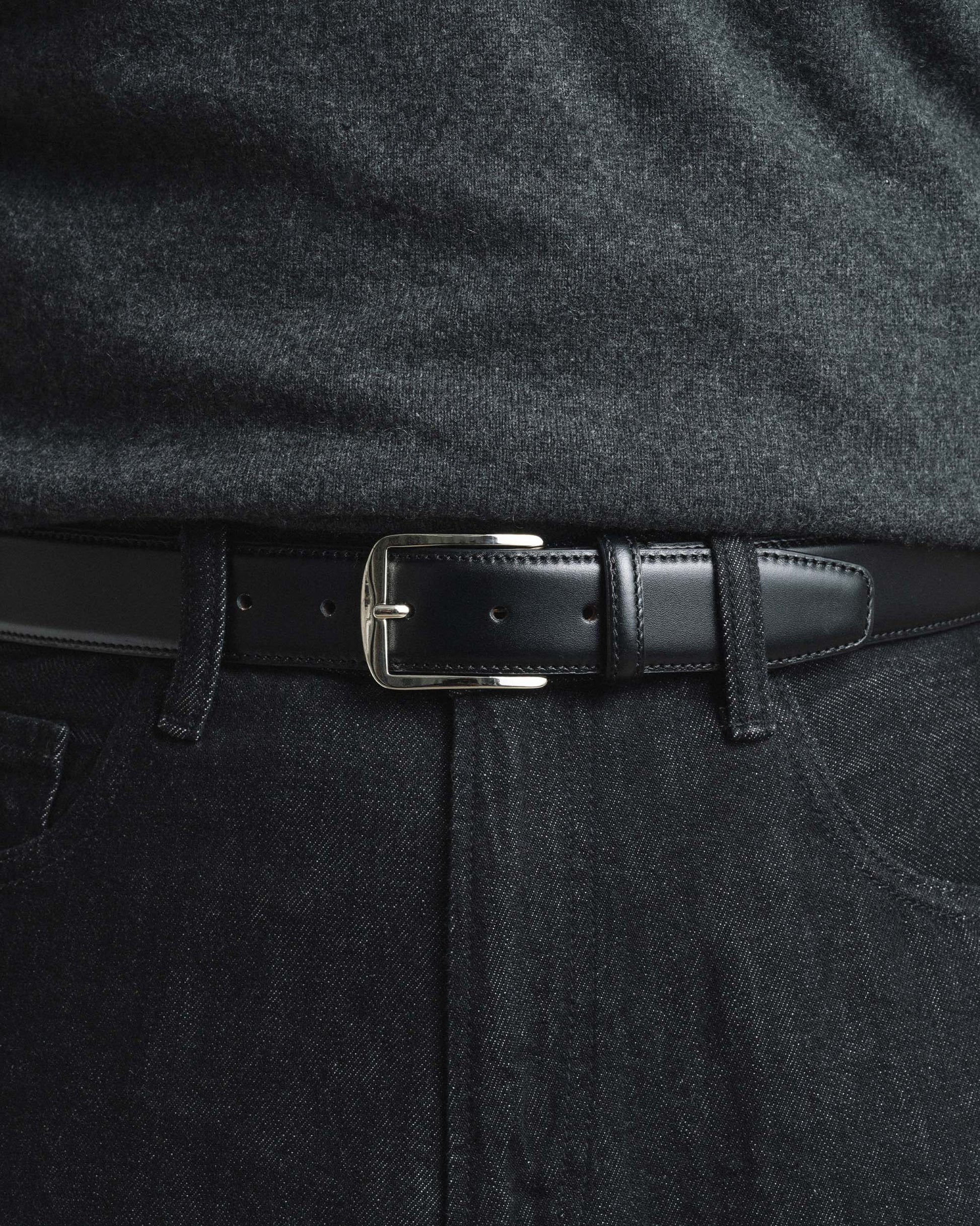 Black leather belt with a square silver buckle, styled with dark denim jeans and a charcoal sweater for a modern, understated look suitable for casual or smart-casual occasions.