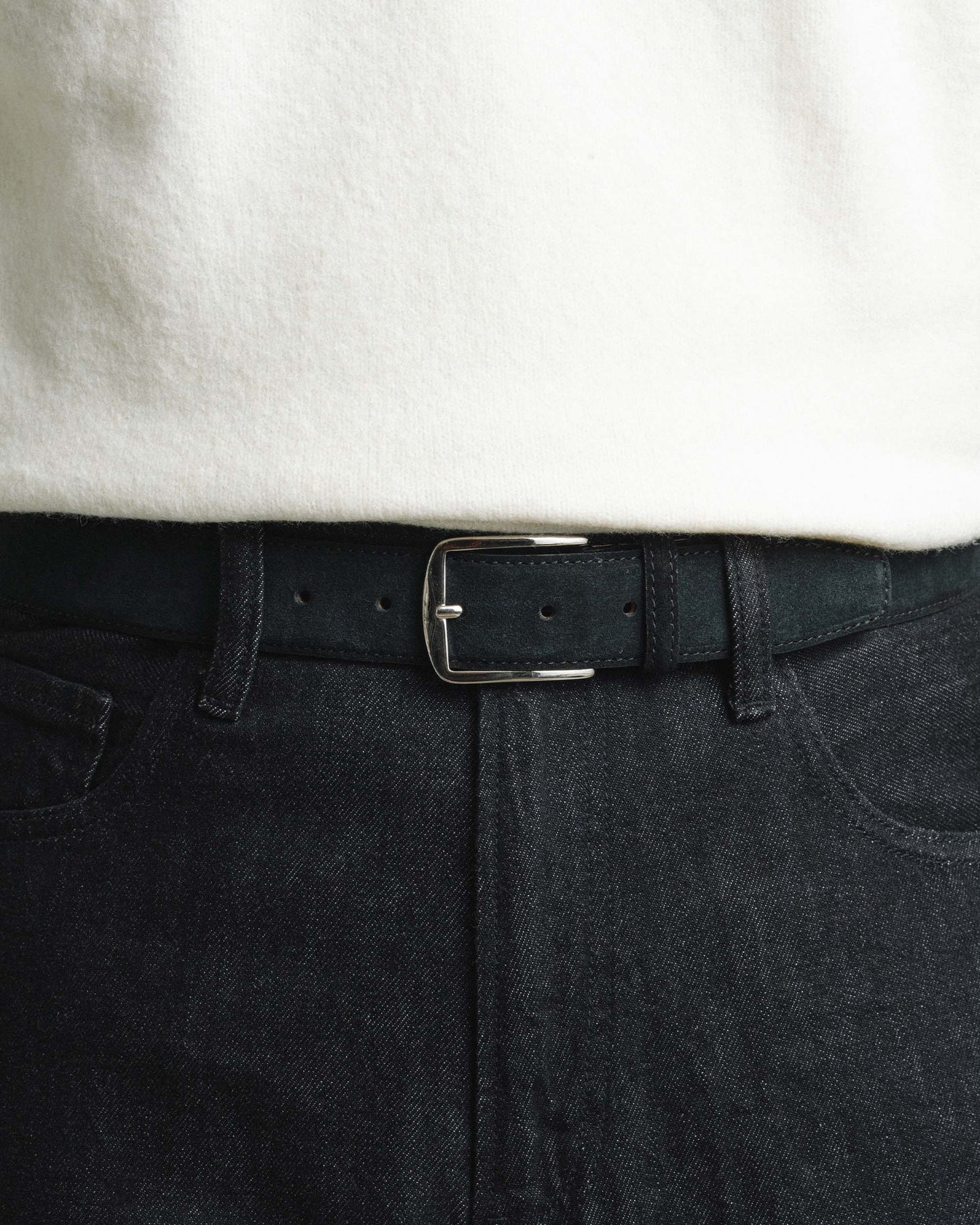 Black suede belt with a silver buckle styled with dark denim jeans and a white shirt, highlighting its refined texture and versatile look for both casual and smart outfits.