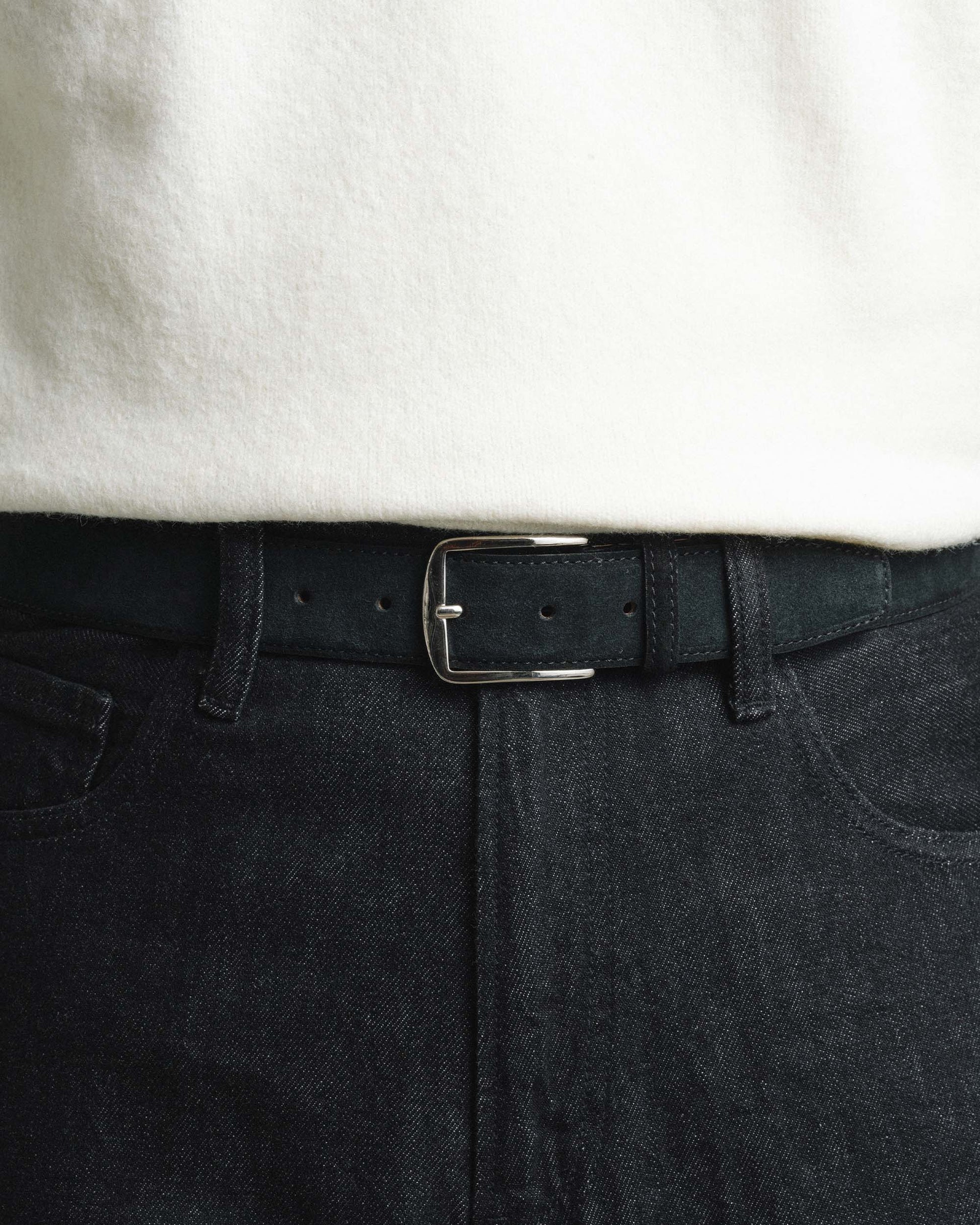 Black suede belt with a silver buckle styled with dark denim jeans and a white shirt, highlighting its refined texture and versatile look for both casual and smart outfits.