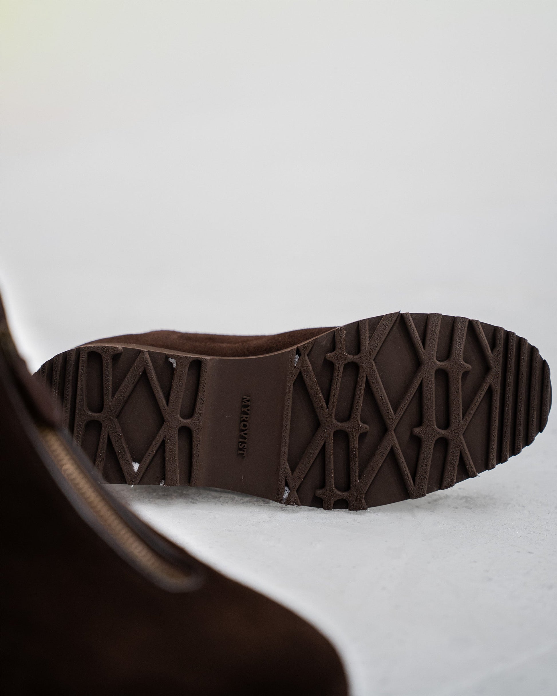 Close-up of the Explorer sole on Funäs in dark brown suede, highlighting the rugged tread pattern designed for grip and stability in winter conditions. The boot’s central zipper and soft suede finish are partially visible, emphasizing both function and refined style.
