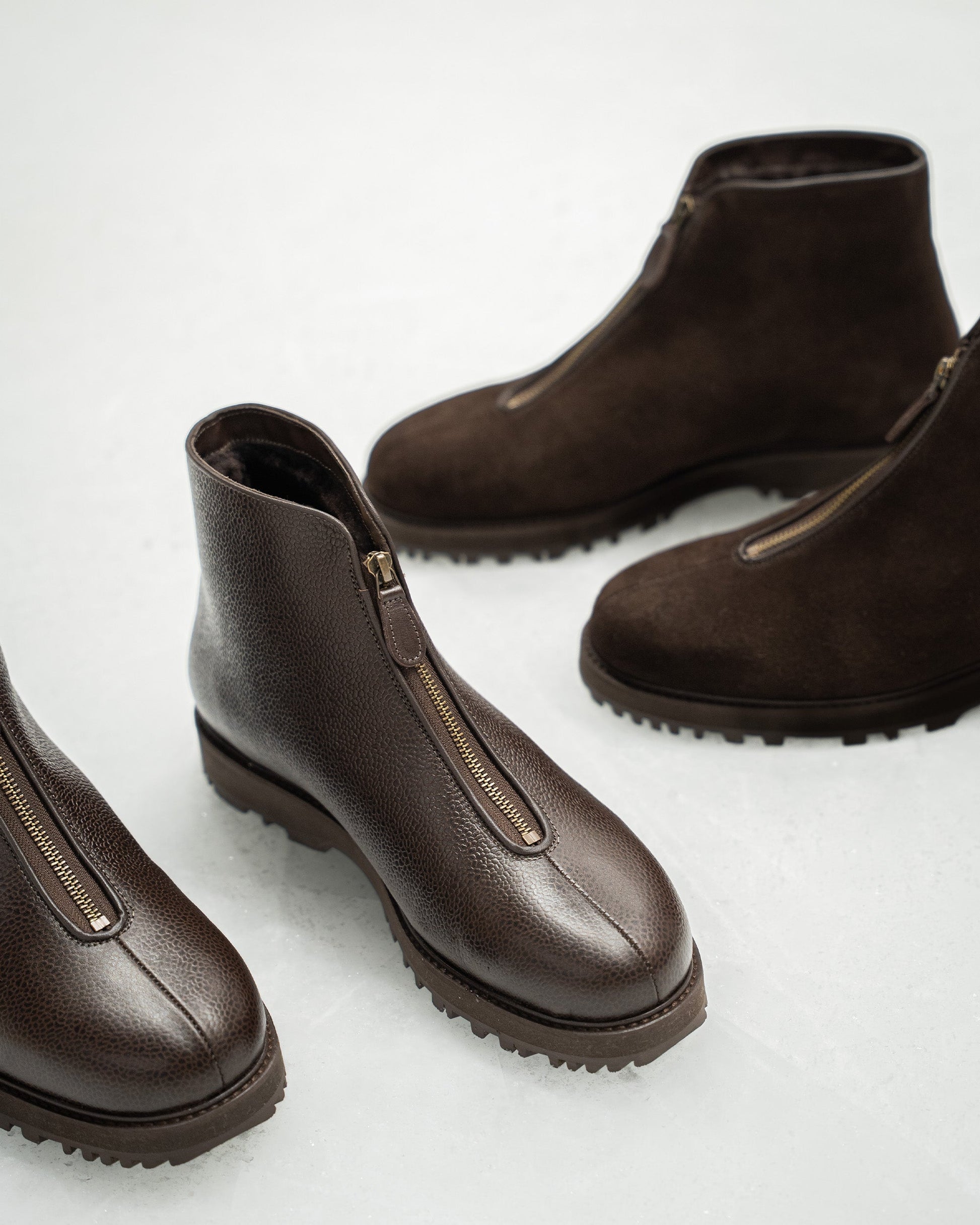 Funäs in dark brown country calf displayed alongside a suede variation, highlighting the textured leather, central zipper, and rugged Explorer sole for versatile winter style.