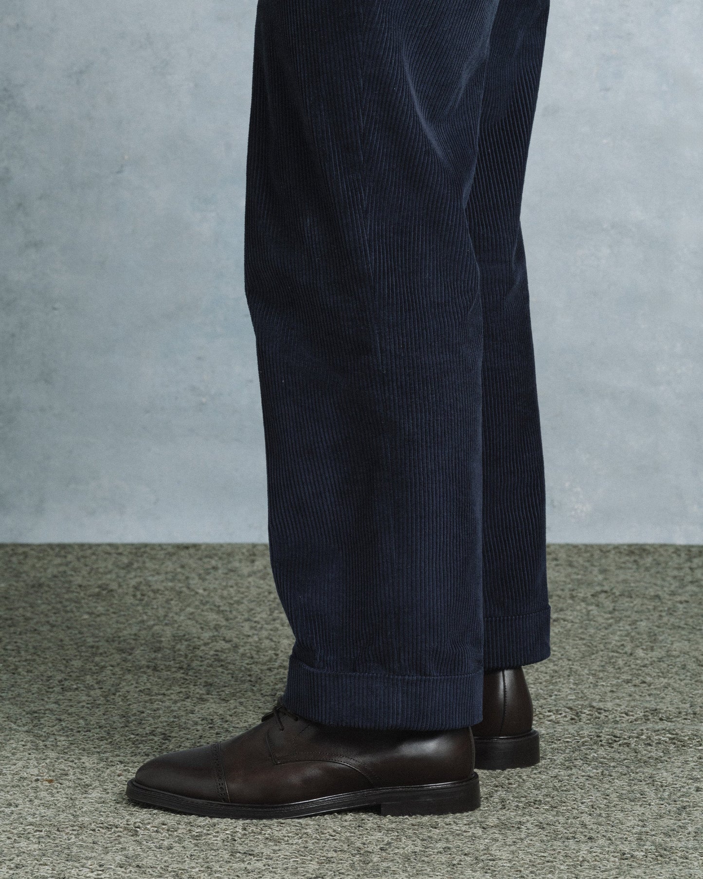 A pair of Tjärnö II in dark brown calf leather boots styled with navy corduroy trousers, highlighting the boot’s rounded toe, subtle broguing, and versatile design for smart casual or business casual outfits.