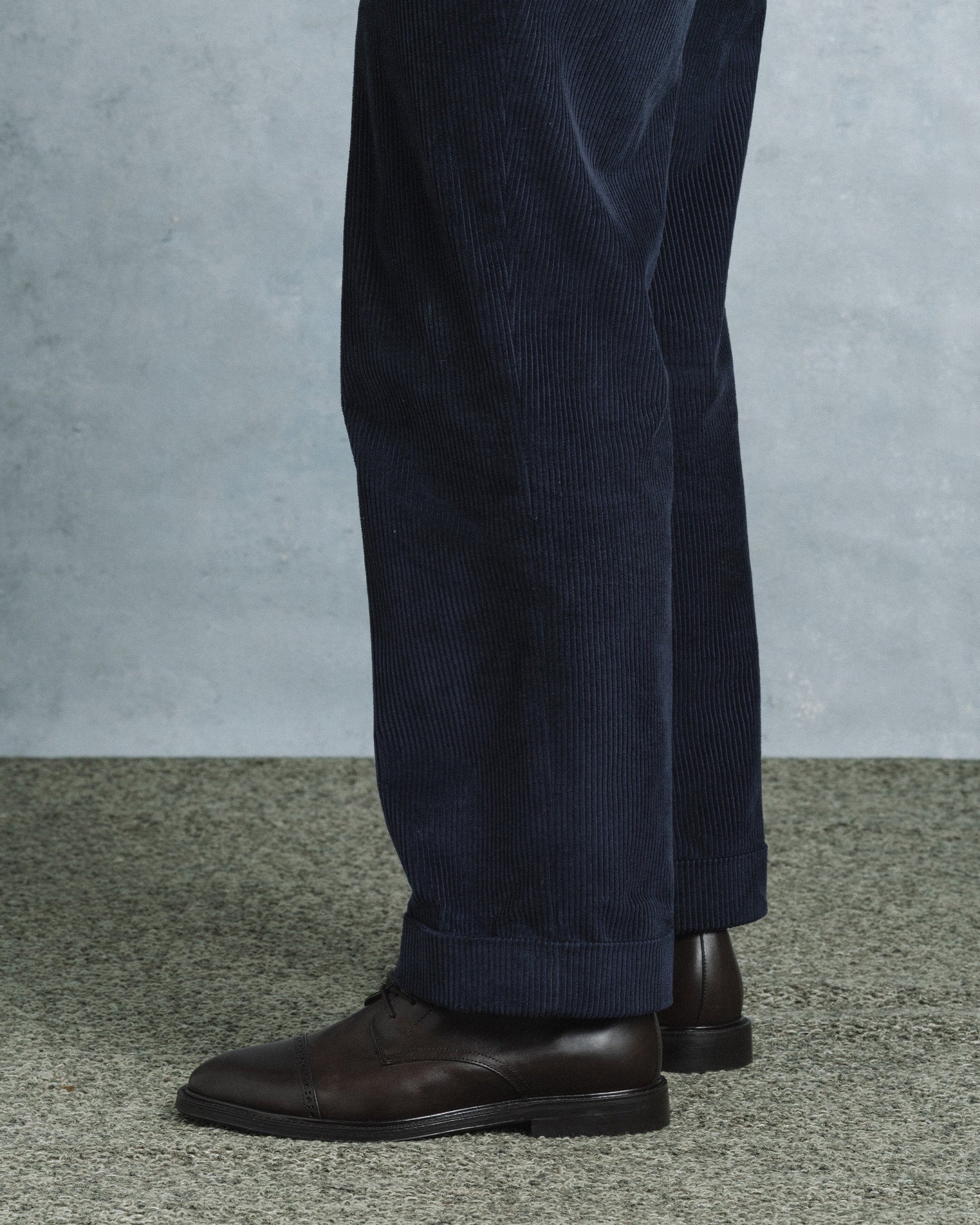 A pair of Tjärnö II in dark brown calf leather boots styled with navy corduroy trousers, highlighting the boot’s rounded toe, subtle broguing, and versatile design for smart casual or business casual outfits.