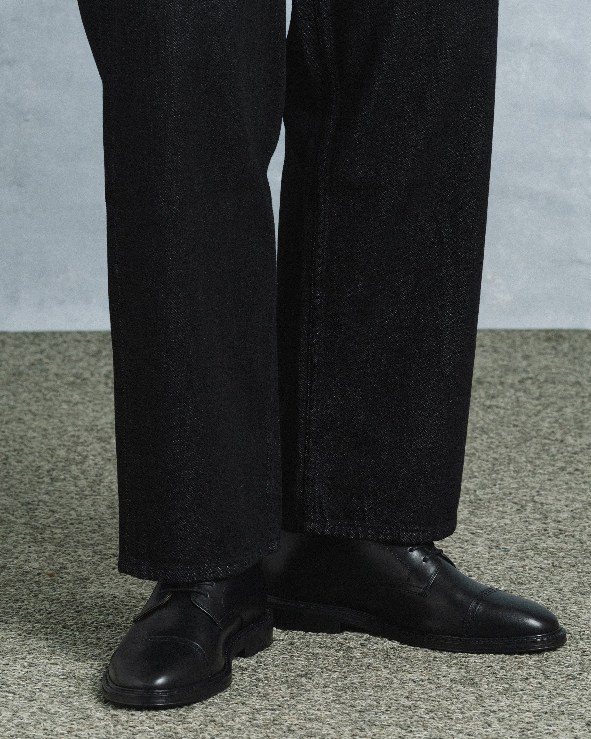 Tjärnö II in black calf styled with dark denim, showcasing the polished cap toe, subtle broguing, and versatile silhouette ideal for both casual and formal outfits.